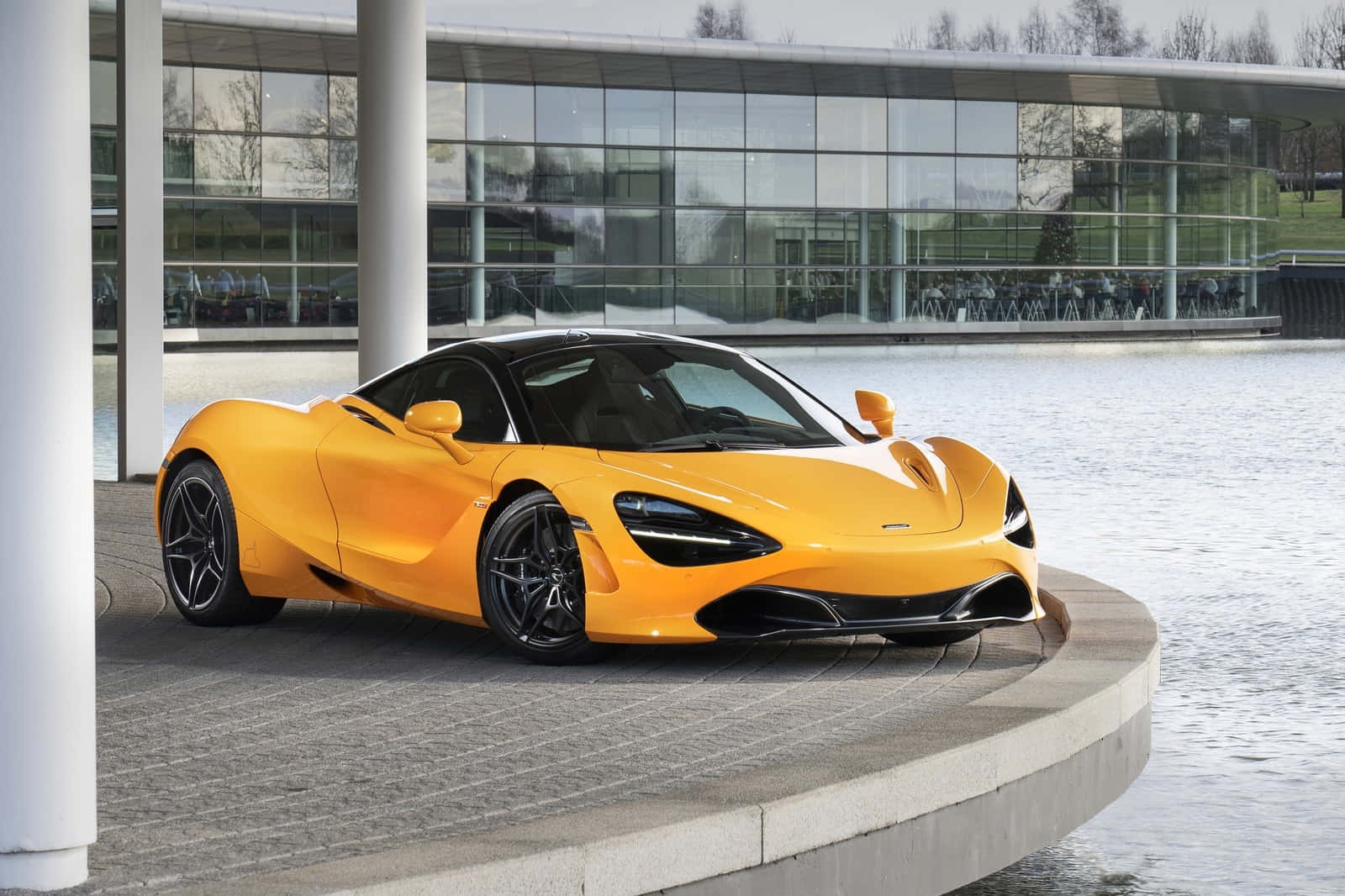 橙色McLaren 720S跑車停泊在玻璃建築旁的水邊。