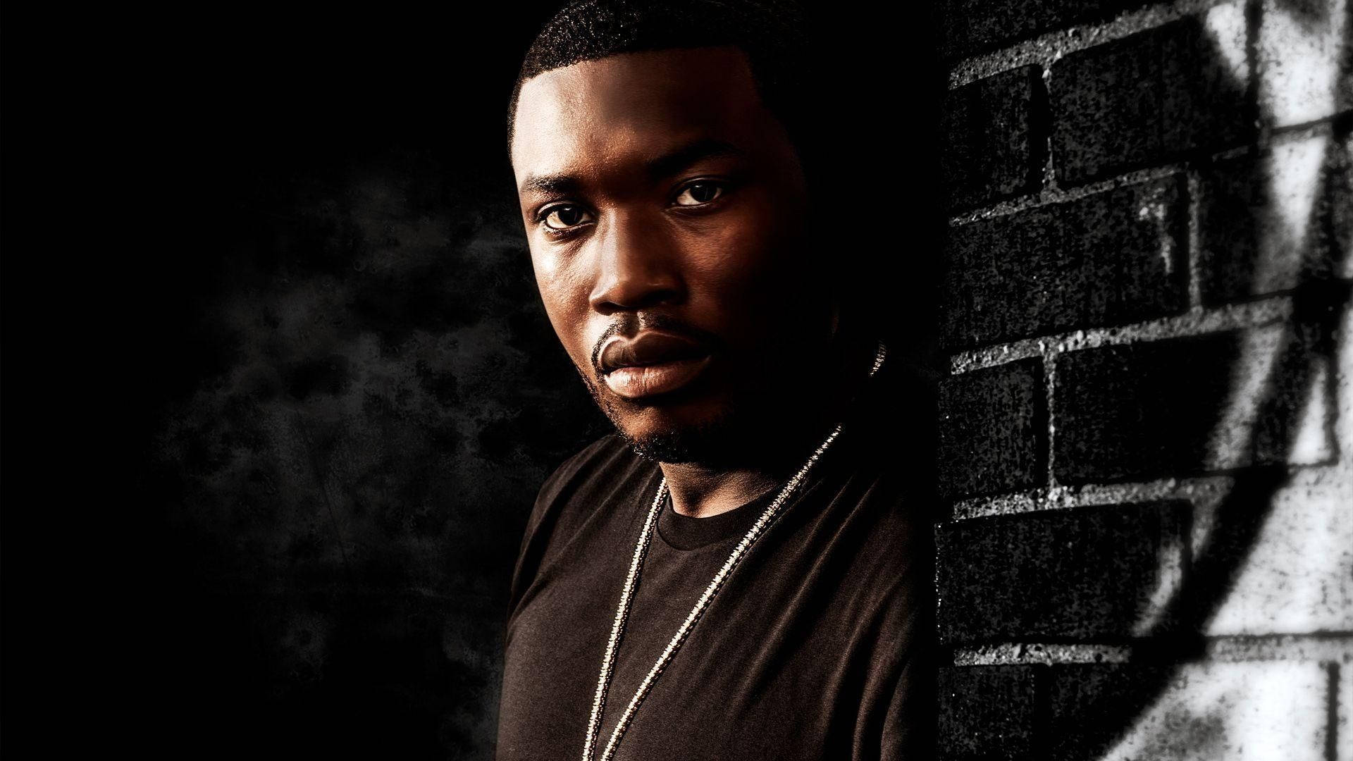 Meek Mill 砖牆倚靠壁紙 壁紙 — 一個表情嚴肅的男人靠在磚牆上，身後煙霧繚繞，形成一幅陰暗憂鬱的肖像。