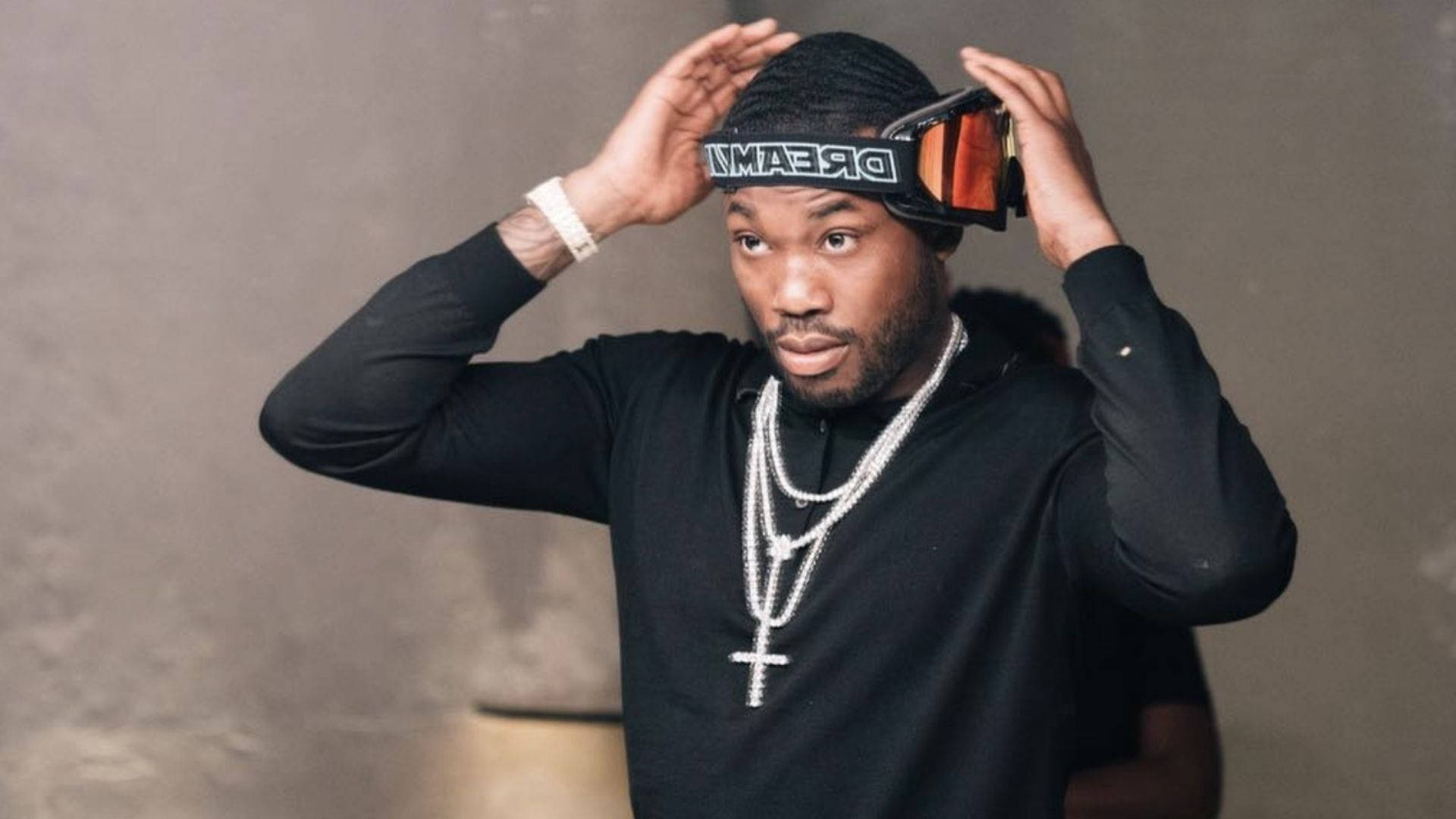 Meek Mill 戴頭盔 壁紙 — 一名身穿黑色服裝的男子在柔和的灰色背景下，戴著多層銀鏈，調整頭上的滑雪護目鏡。
