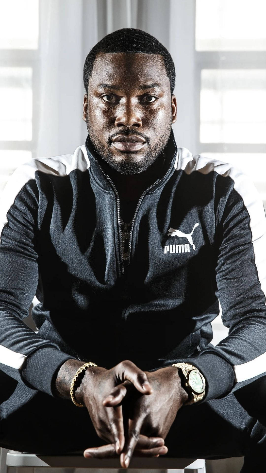 Meek Mill 穿 Puma 壁紙 — 一名身穿黑白Puma運動服的男子自信地坐在明亮的窗戶背景前，雙手緊握。