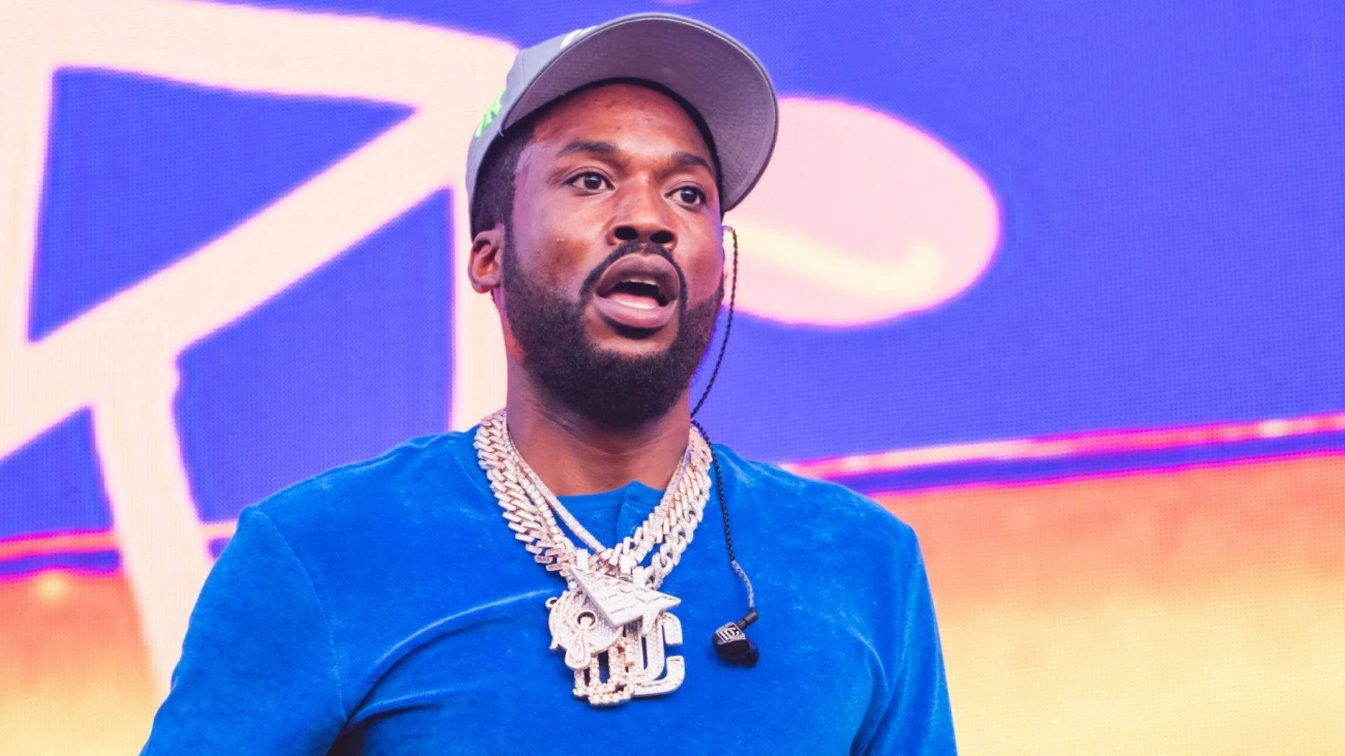 Meek Mill 藍色上衣演出照 壁紙 — 一名留鬍鬚、戴帽子的男士在台上熱情演講，身穿藍色襯衫和粗金鏈。