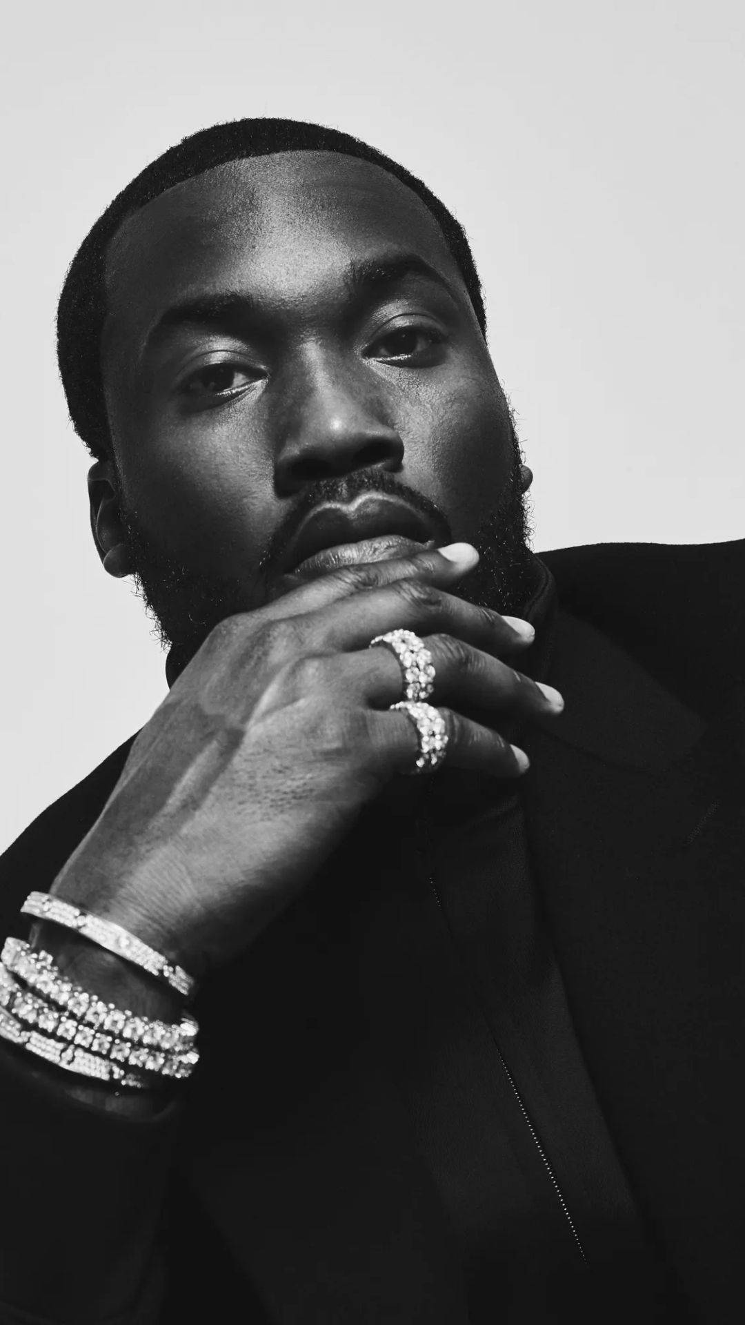 Meek Mill 黑白照 壁紙 — 一個鬍鬚男的黑色肖像，戴著鑽石戒指和手鐲，手托下巴，背景簡潔。