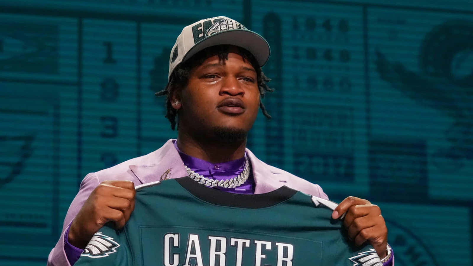  壁紙 — 一名美式足球員自豪地舉起一件前面印有「CARTER」的綠色Eagles球衣，同時戴著相配的帽子和紫色西裝。