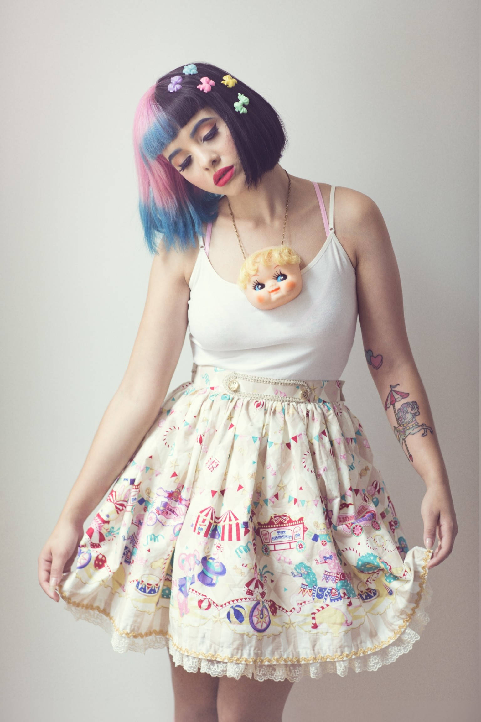 Melanie Martinez 糖果髮夾 壁紙 — 一位年輕女性，擁有色彩繽紛的頭髮和一條古怪圖案的裙子，在純色背景前擺姿勢。