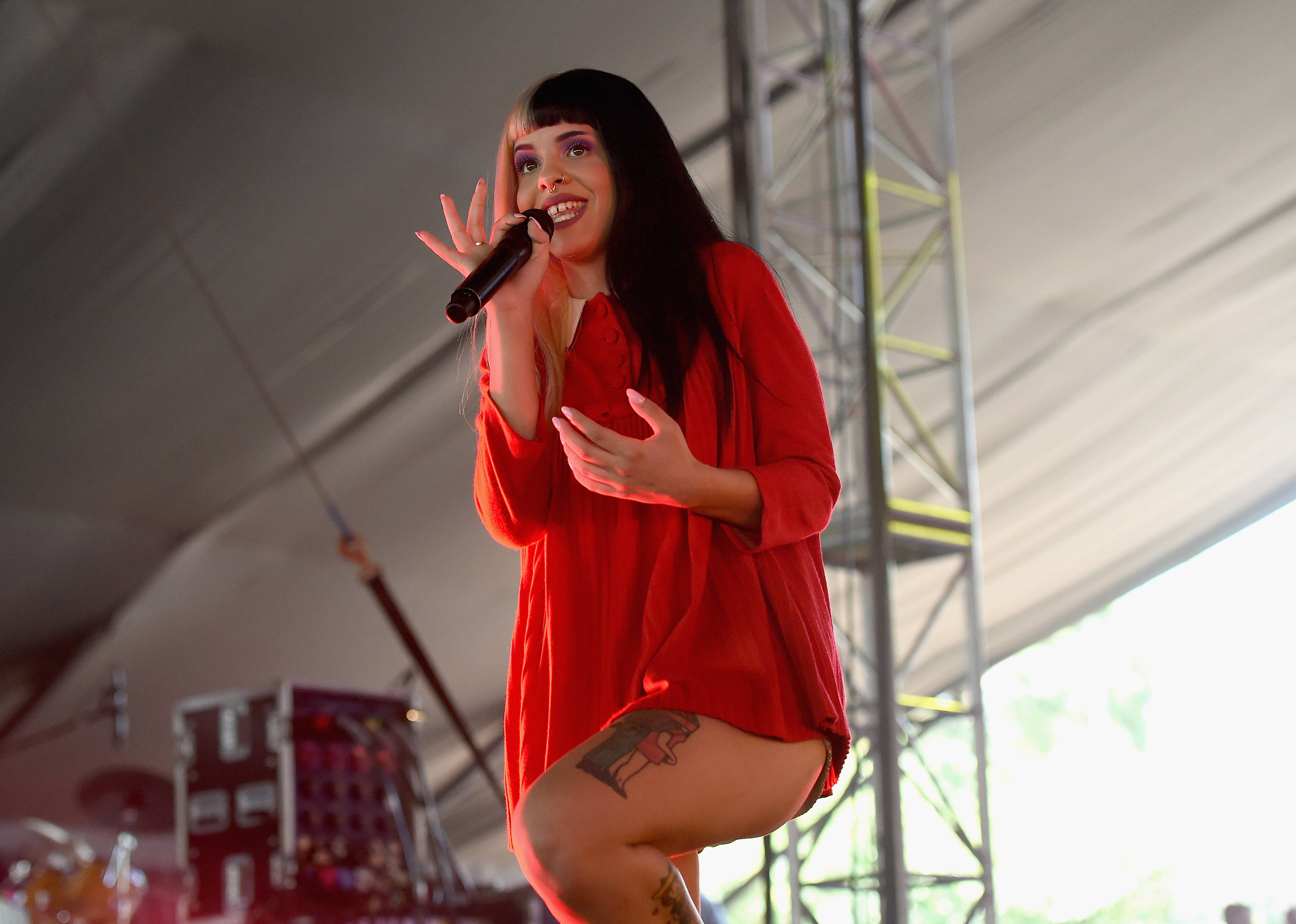 Melanie Martinez 紅色上衣 壁紙 — 一位微笑的歌手穿著紅色連衣裙，在帳篷舞台上手持麥克風充滿活力地表演。