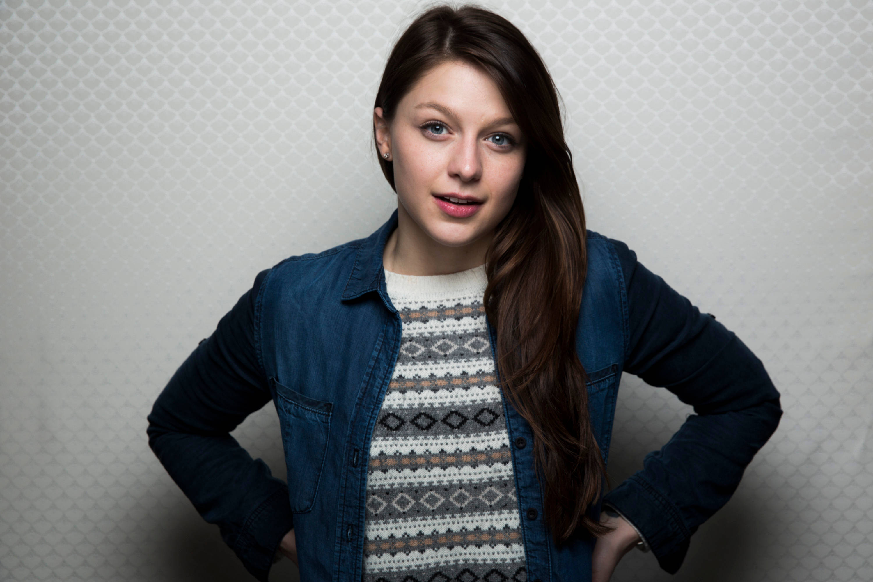 Melissa Benoist 牛仔外套造型 壁紙 — 一位年輕女性留著長長嘅棕色頭髮，自信地企喺有紋理嘅白色牆前面，身穿牛仔外套，入面係一件圖案毛衣。
