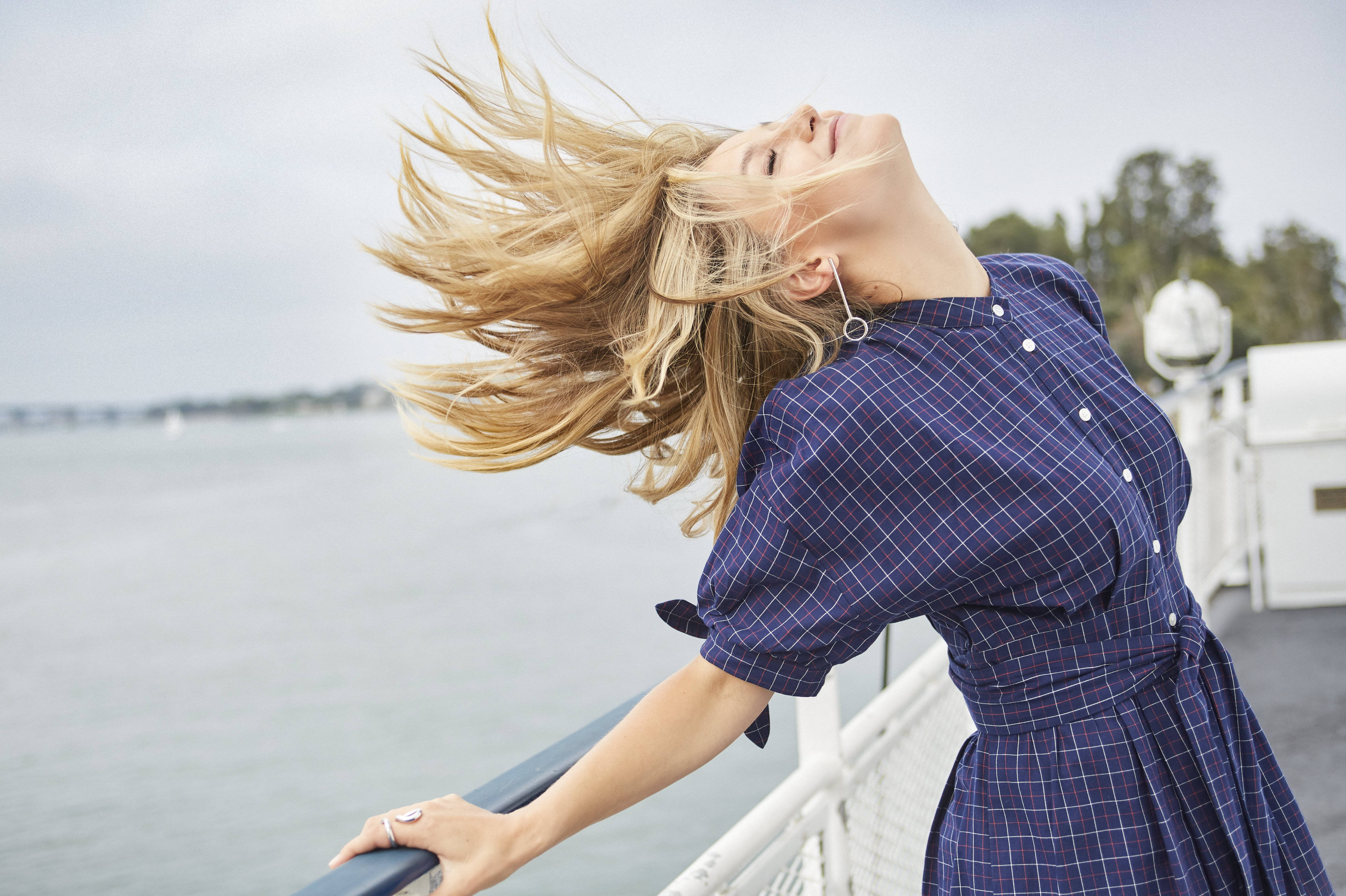 Melissa Benoist 風中飄逸秀髮 壁紙 — 一位擁有飄逸金髮的女性靠在船欄杆上，閉著眼睛，享受水面上的微風。