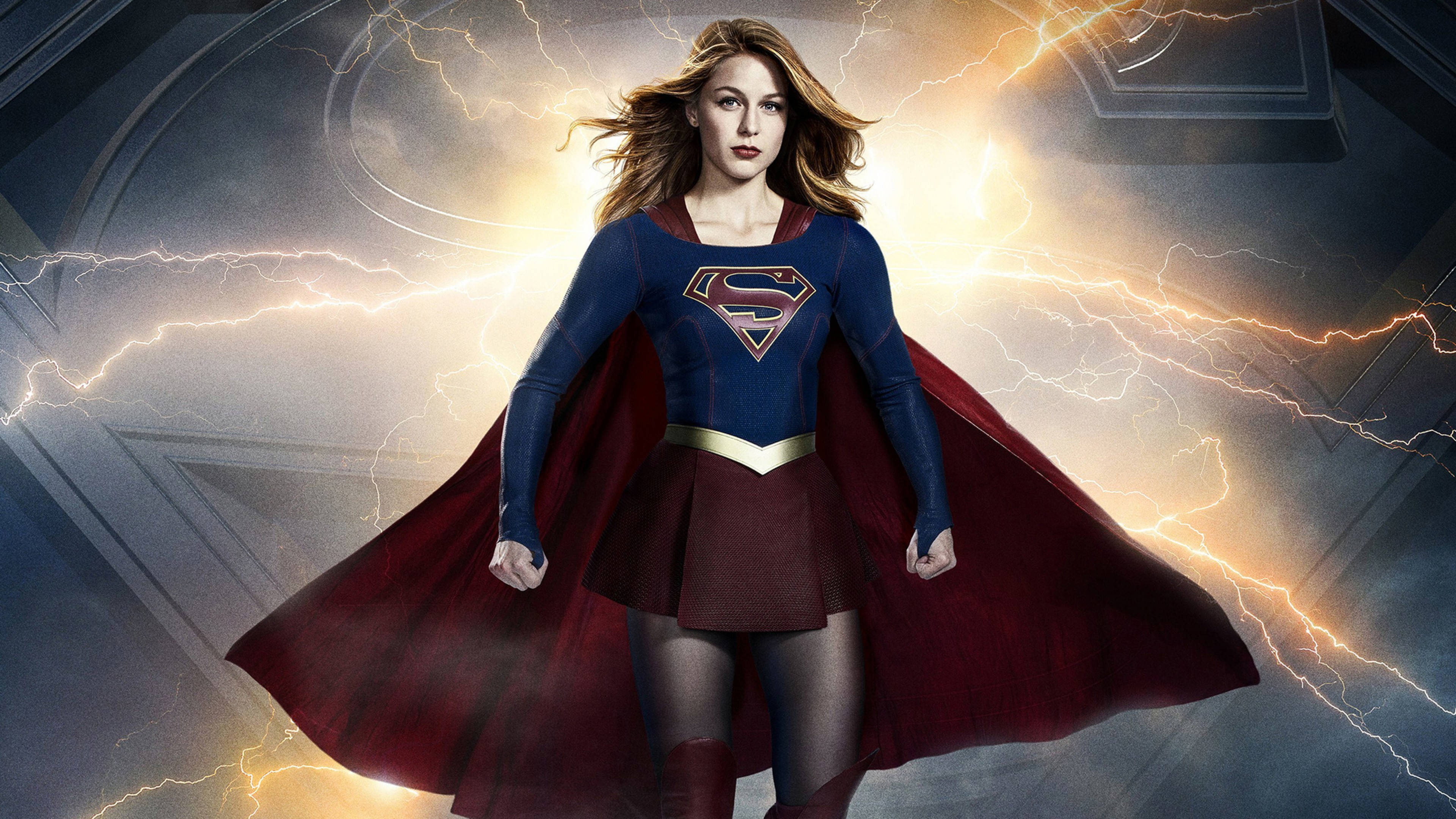 Melissa Benoist 飾演超級女孩 DC 英雄 壁紙 — 超級女孩以動感姿勢英勇站立，閃電在她周圍噼啪作響，營造出戲劇性的電影場景。