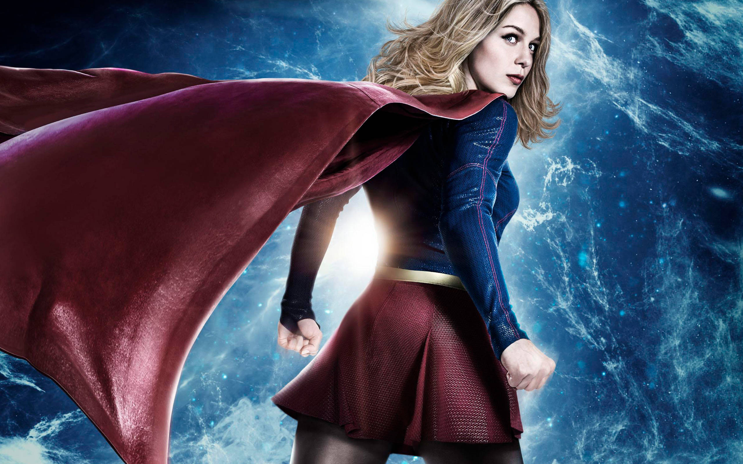 Melissa Benoist 經典超級女孩造型 壁紙 — 一位擁有飄逸金髮和紅色斗篷的女超級英雄，在宇宙藍色能量背景下蓄勢待發。