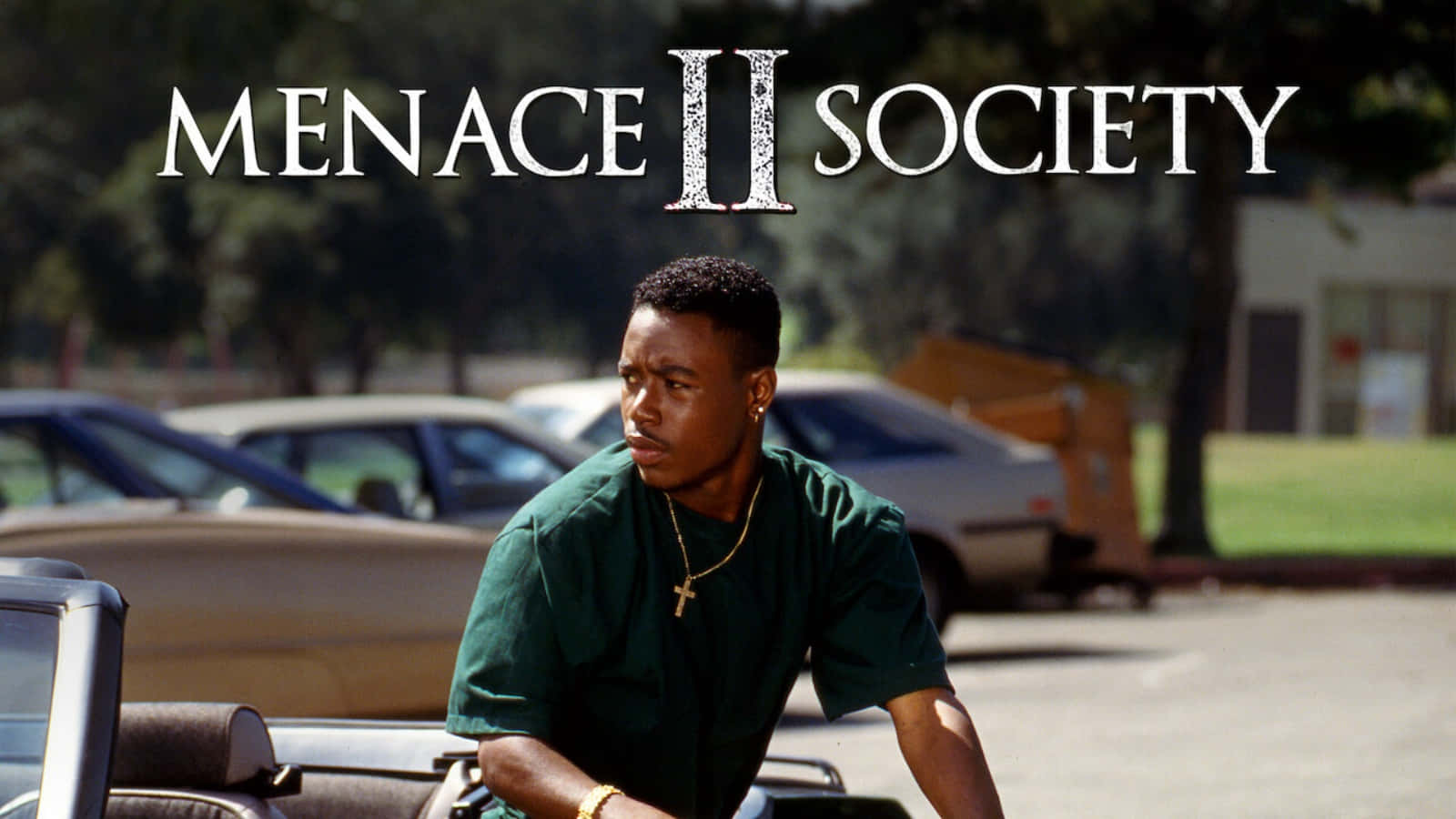《Menace II Society》中的Caine與O-Dog 壁紙 — 一名身穿綠色襯衫的年輕男子在陽光明媚的停車場靠在一輛車上，上方有「Menace II Society」的標題。