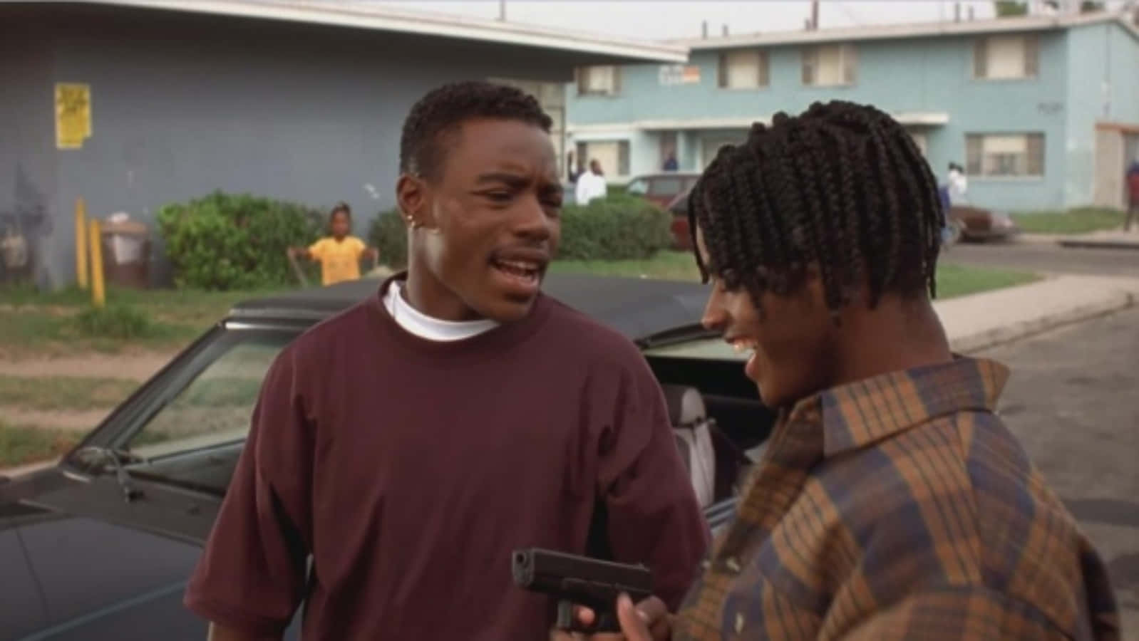 《Menace II Society》卡恩與O-Dog持槍對話 壁紙 — 兩名男子在戶外對峙，手槍靠近對方臉部，場面緊張的街頭場景。