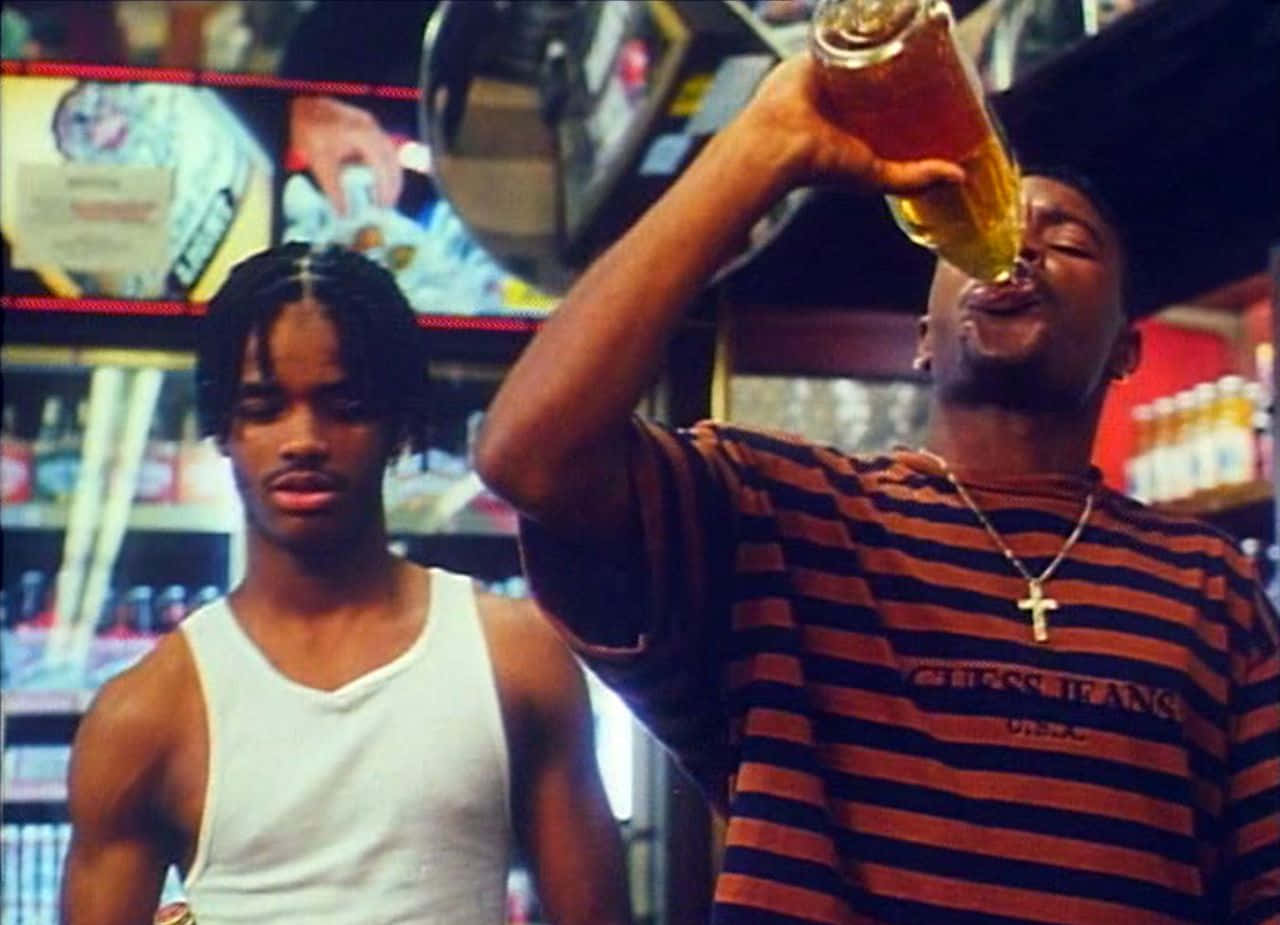 《Menace II Society》Caine與O-Dog於店內飲酒 壁紙 — 兩個年輕男子在燈光昏暗的酒吧裡，一個在喝啤酒，另一個則面帶嚴肅地直視前方。