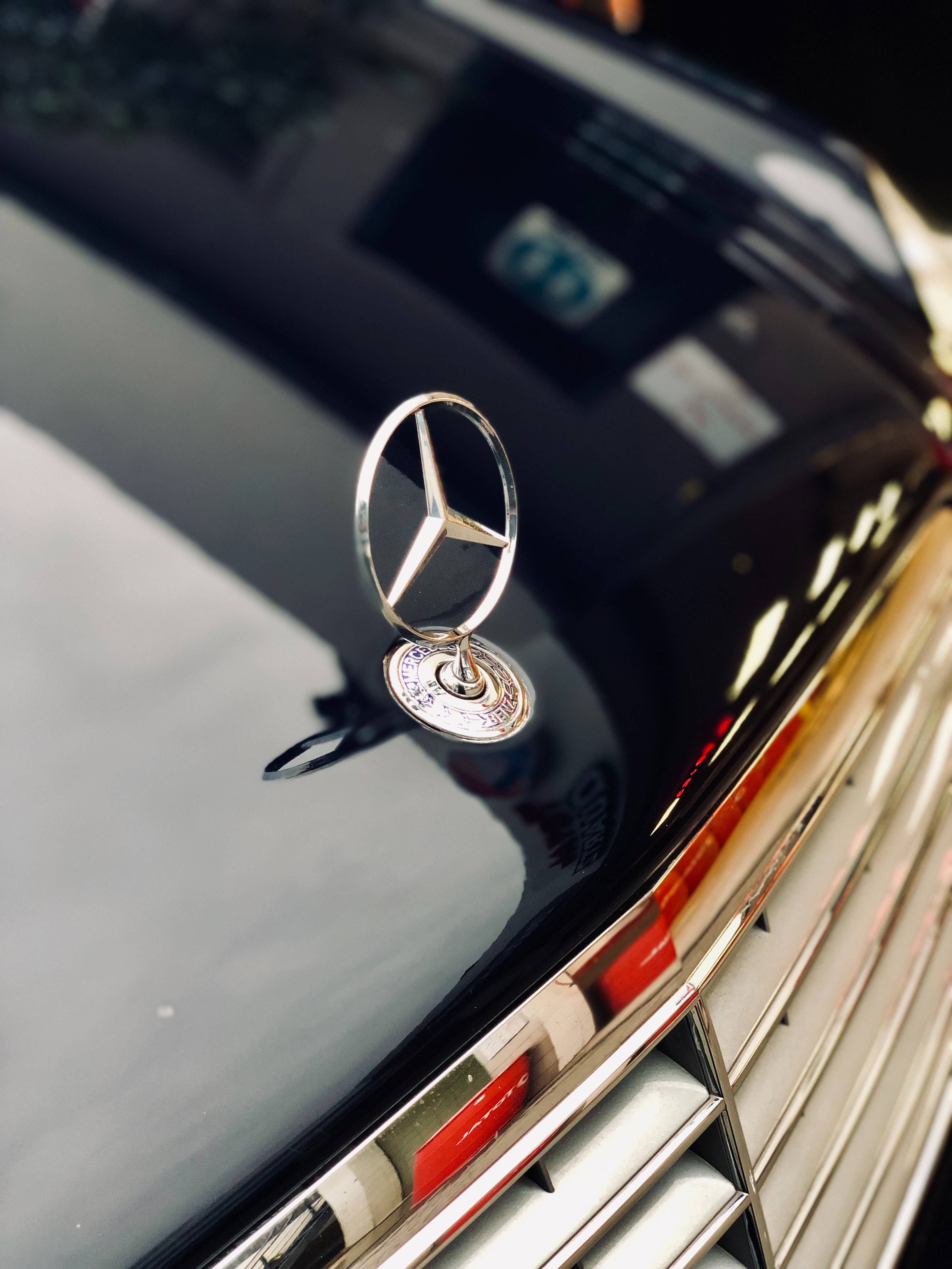 光澤黑 Mercedes-Benz 車標 壁紙 — 特寫：閃亮銀色 Mercedes-Benz 引擎蓋飾件，置於帶有鍍鉻飾條的亮黑色引擎蓋上。