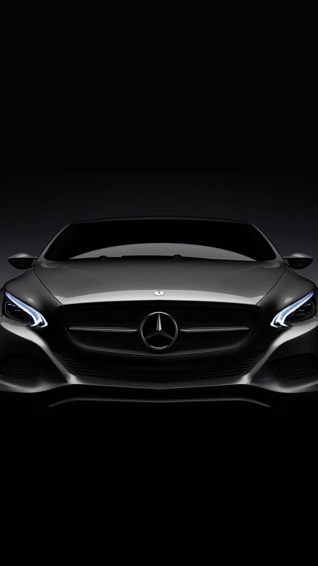 時尚黑色 Mercedes-Benz iPhone 壁紙 — 一輛時尚黑色平治汽車的前視圖，帶有發光的車頭燈，背景為深色。