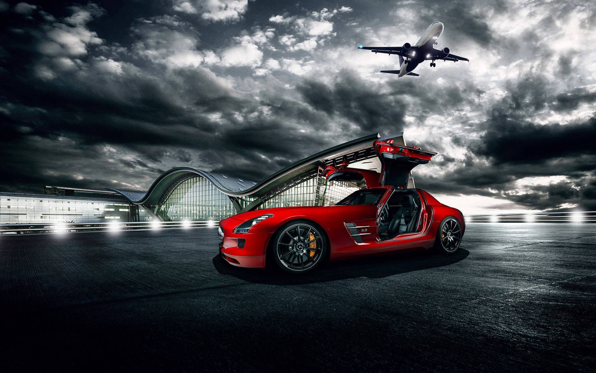 紅色Mercedes-Benz SLS AMG 壁紙 — 一輛引人注目的紅色鷗翼門跑車停在黑暗的停機坪上，一架飛機在暴風雨的天空下飛過。