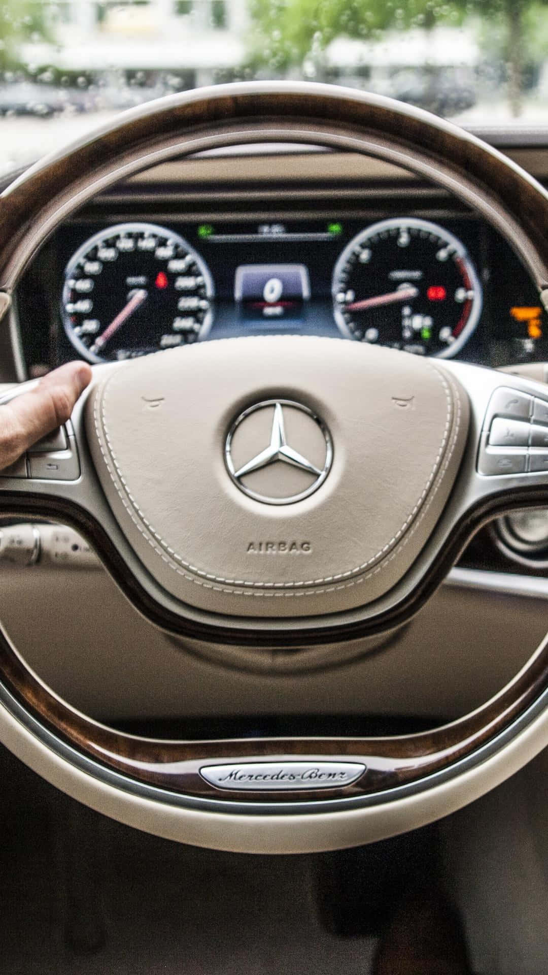 手放在 Mercedes-Benz 方向盤上，帶有木質飾邊和數位儀表板。