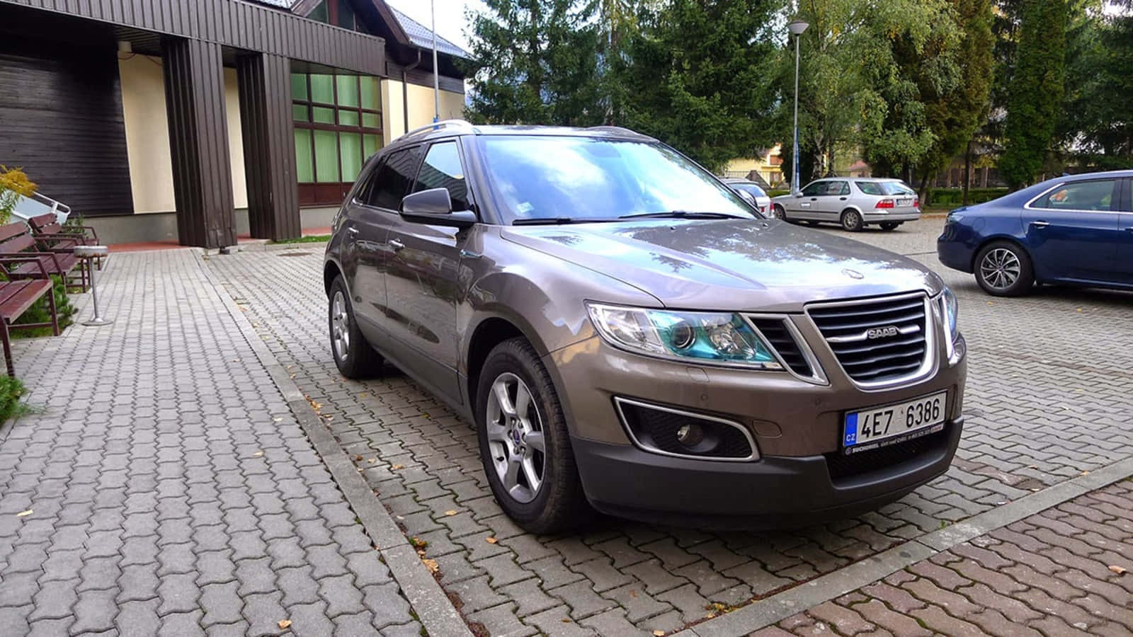 Saab 9-4x 桌布 壁紙 — 一輛金屬啡色薩博SUV停泊在灰色磚砌車道上，旁邊是一座帶綠色窗戶的現代建築。