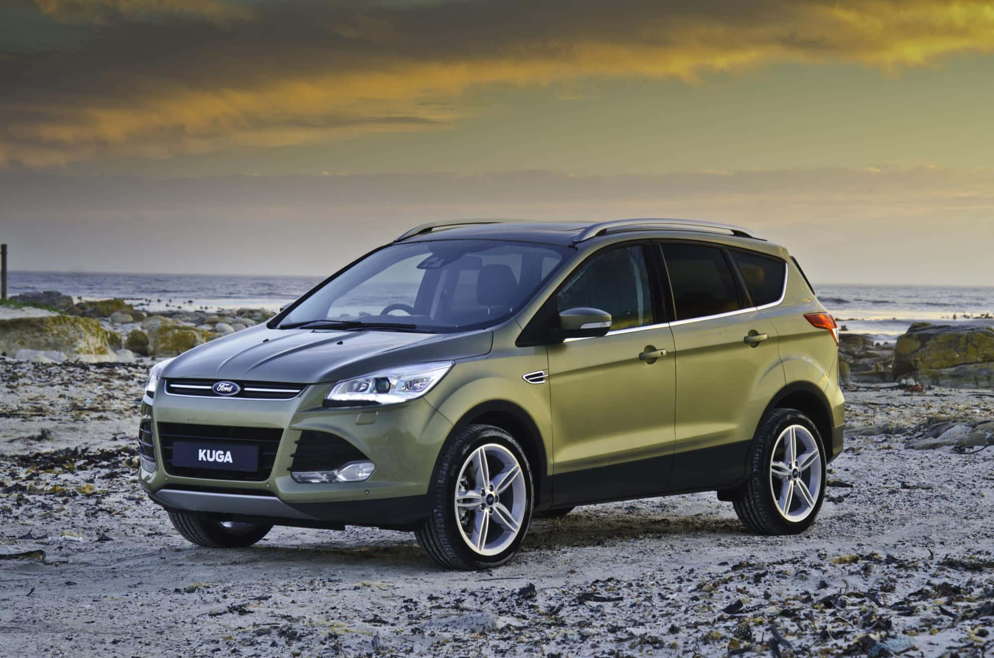 Ford Escape 桌布 壁紙 — 一輛金屬綠色的福特 Kuga SUV 停泊在日落時分的岩石海灘上，上方有戲劇性的雲層。