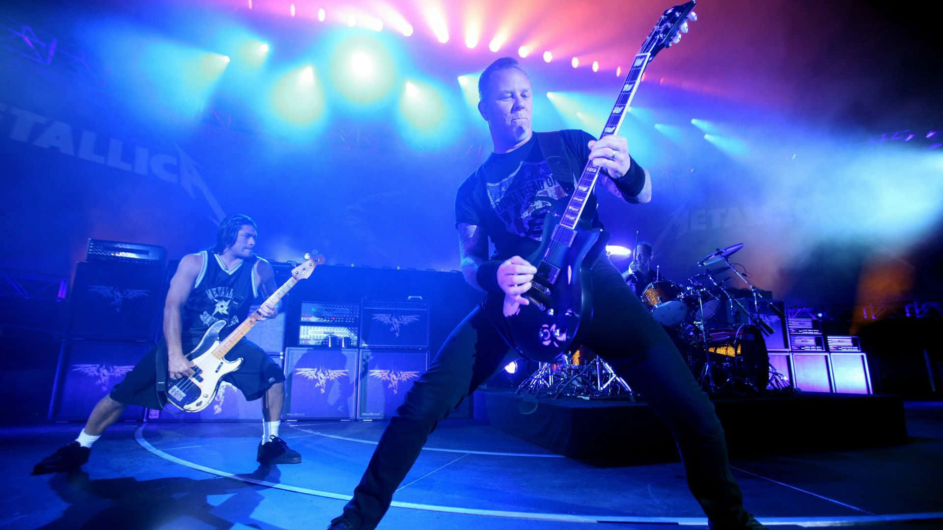 Metallica 樂隊在色彩繽紛的舞台上進行現場表演，燈光強烈。