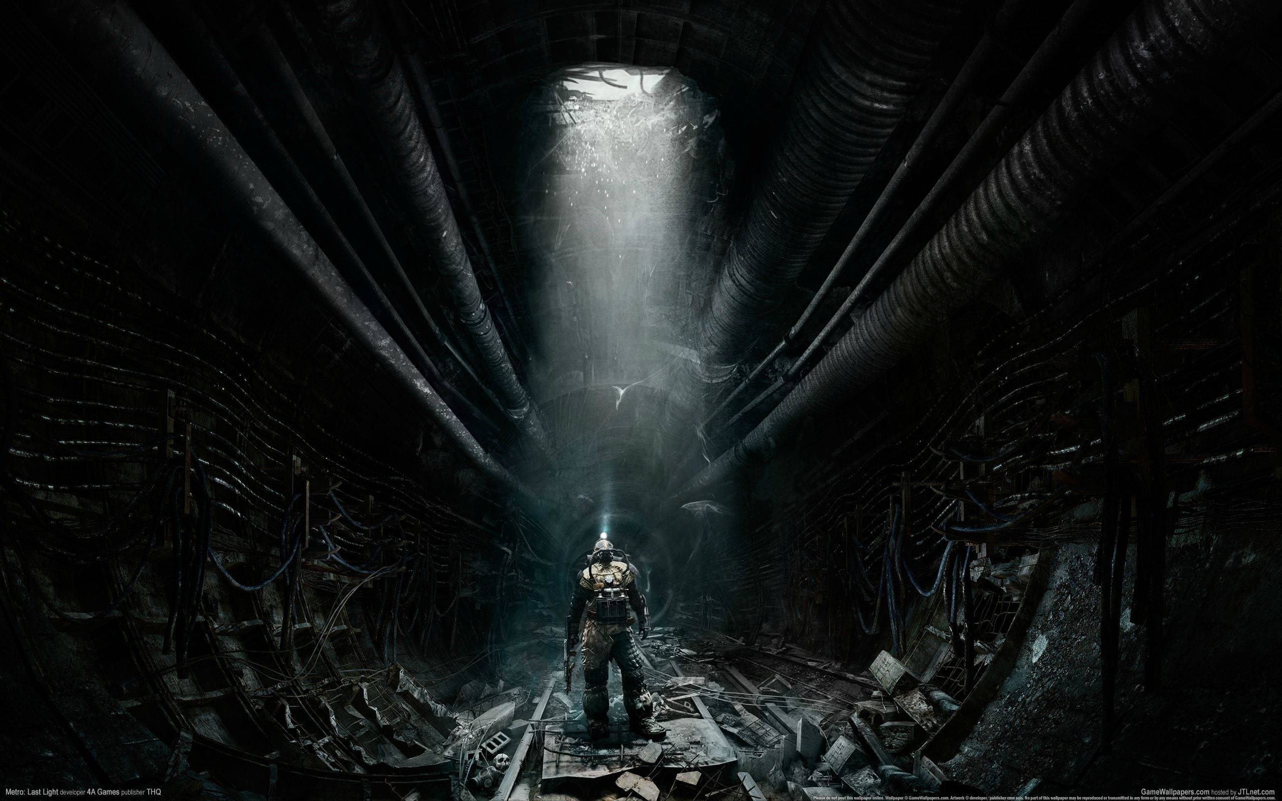 《Metro Exodus》毀損隧道 壁紙 — 一個孤獨的裝甲人物站在黑暗的工業隧道中，一道光束從上方天花板穿透而下。