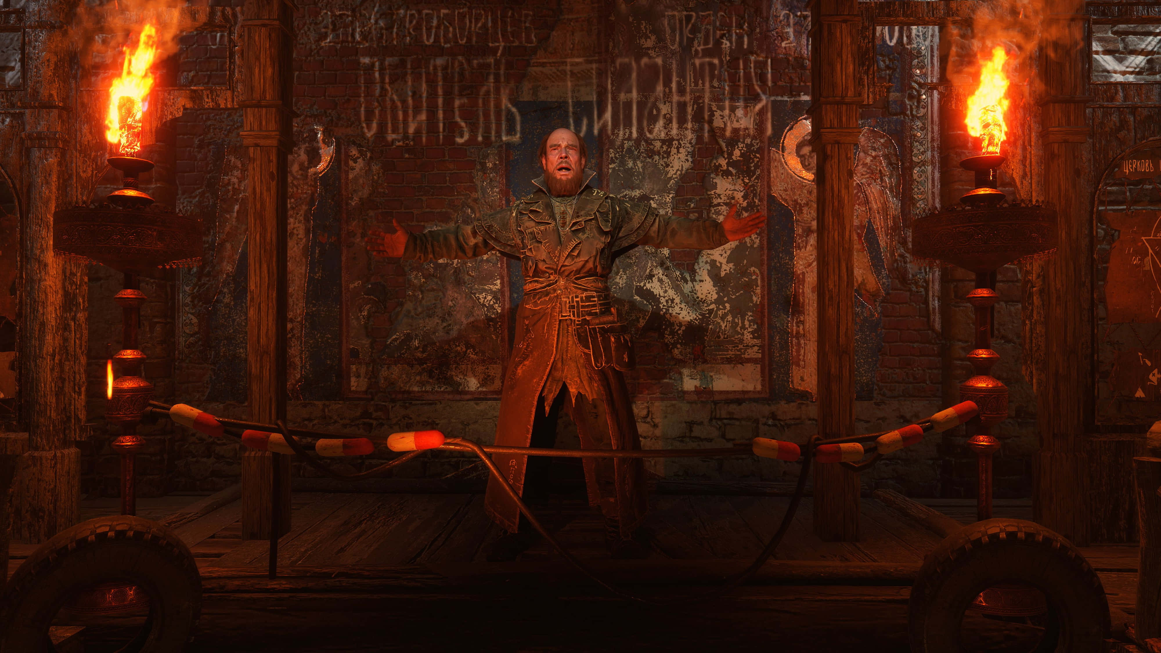 沉浸在《Metro Exodus》不斷演變的末日世界 壁紙 — 一個穿著破爛外套的男人在一個火光熊熊、火炬照亮、佈滿塗鴉的房間裡張開雙臂站立。