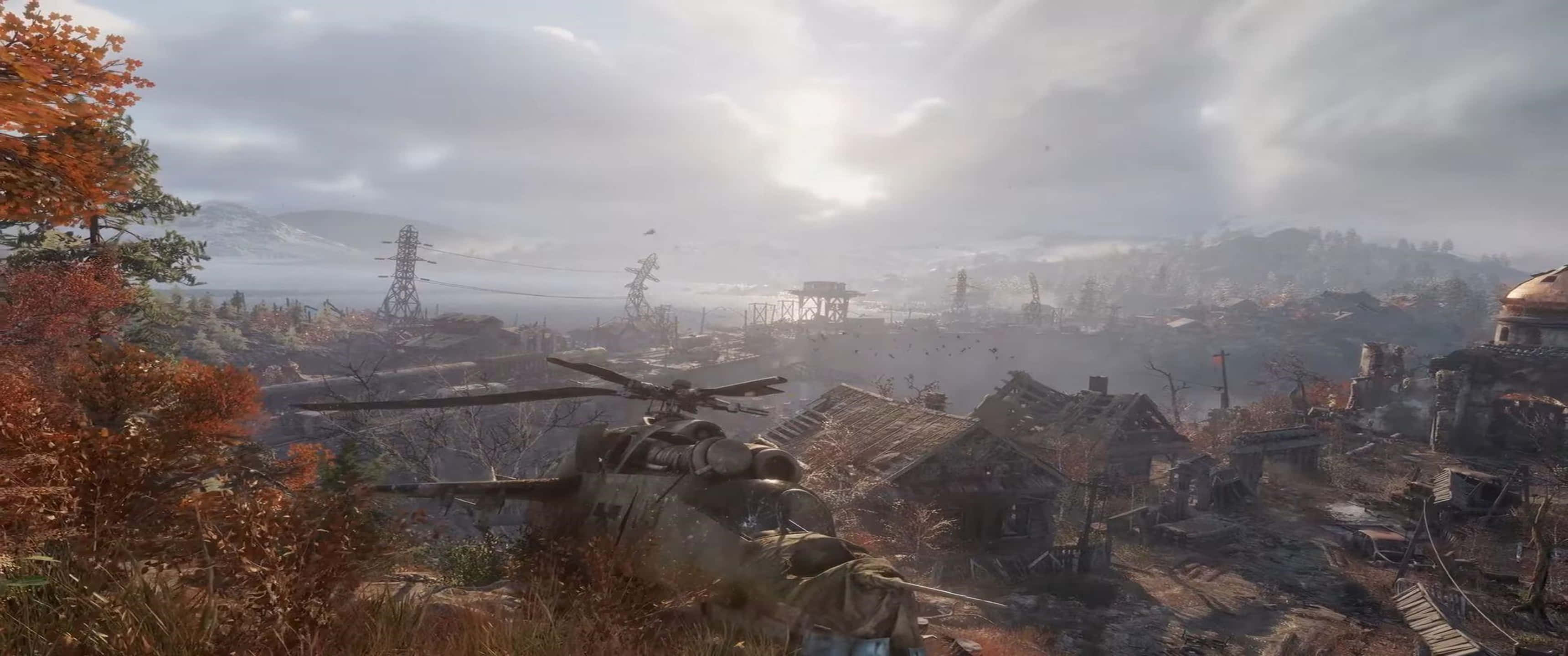 《Metro Exodus》遊戲中毀損的直升機 3440x1440p 背景 壁紙 — 一架墜毀的直升機在廢墟建築物和秋樹之間，在朦朧多雲的天空下靜止不動。