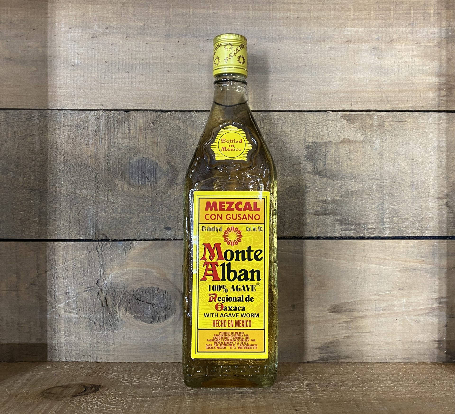 蒙特阿爾班mezcal龍舌蘭酒置於木牆旁 壁紙 — 一瓶蒙特阿爾班梅斯卡爾酒連同龍舌蘭蟲，置於質樸木板上，在柔和自然光下居中擺放。