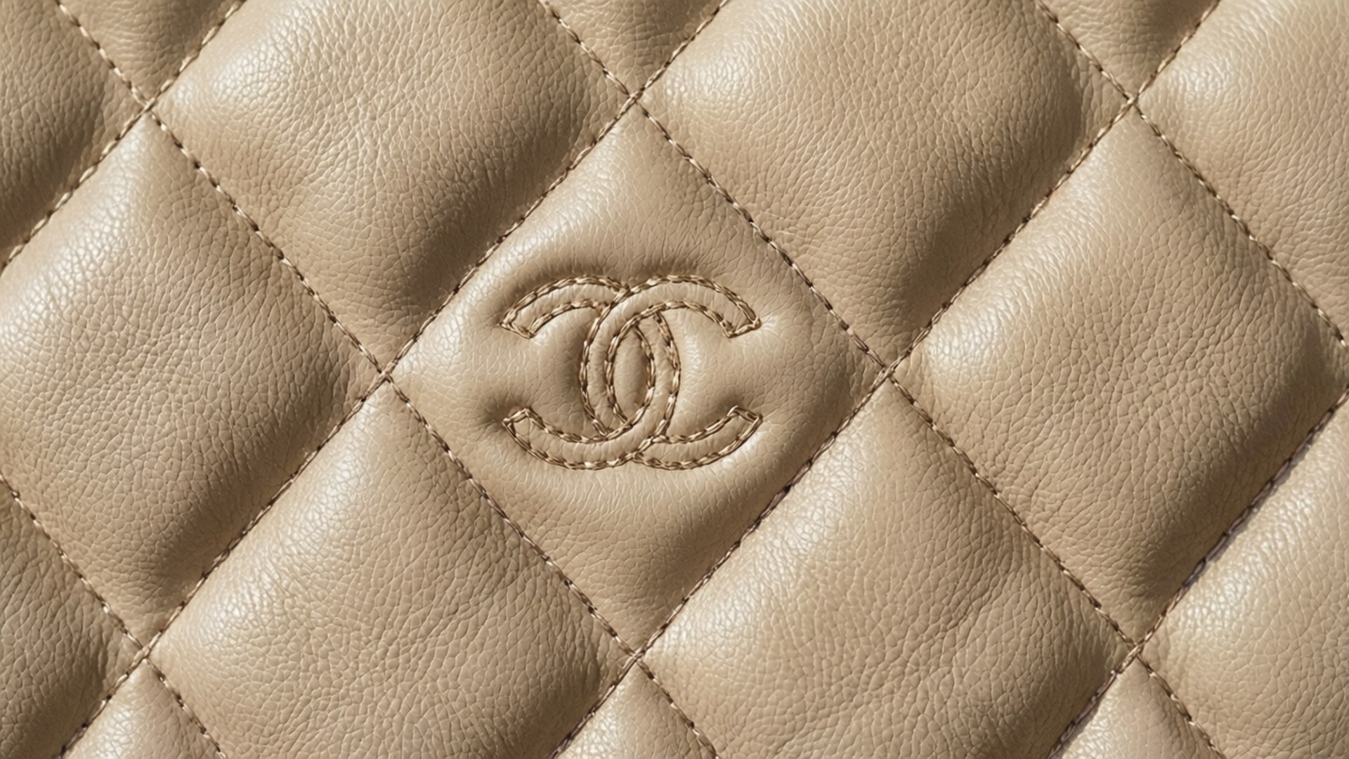Chanel 桌布 壁紙 — 米色絎縫皮革特寫，中央菱形圖案有縫製的 Chanel 標誌。