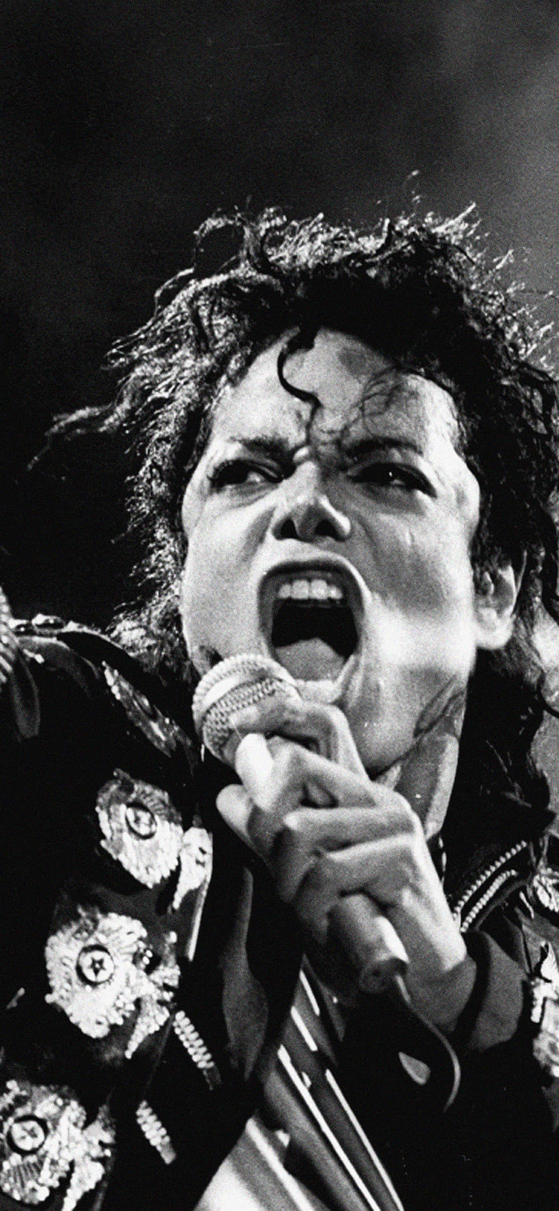 《Michael Jackson iPhone》——讓音樂節奏帶你舞動 壁紙 — 米高積遜在黑白的高能量現場表演中，充滿激情地對著咪高峰唱歌。