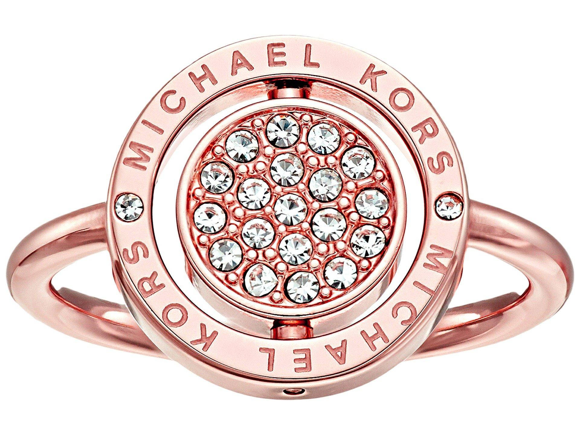 Michael Kors 玫瑰金鑽石手鐲 壁紙 — 玫瑰金色Michael Kors戒指，圓形戒環刻有品牌名稱，中央飾有閃爍水晶簇。