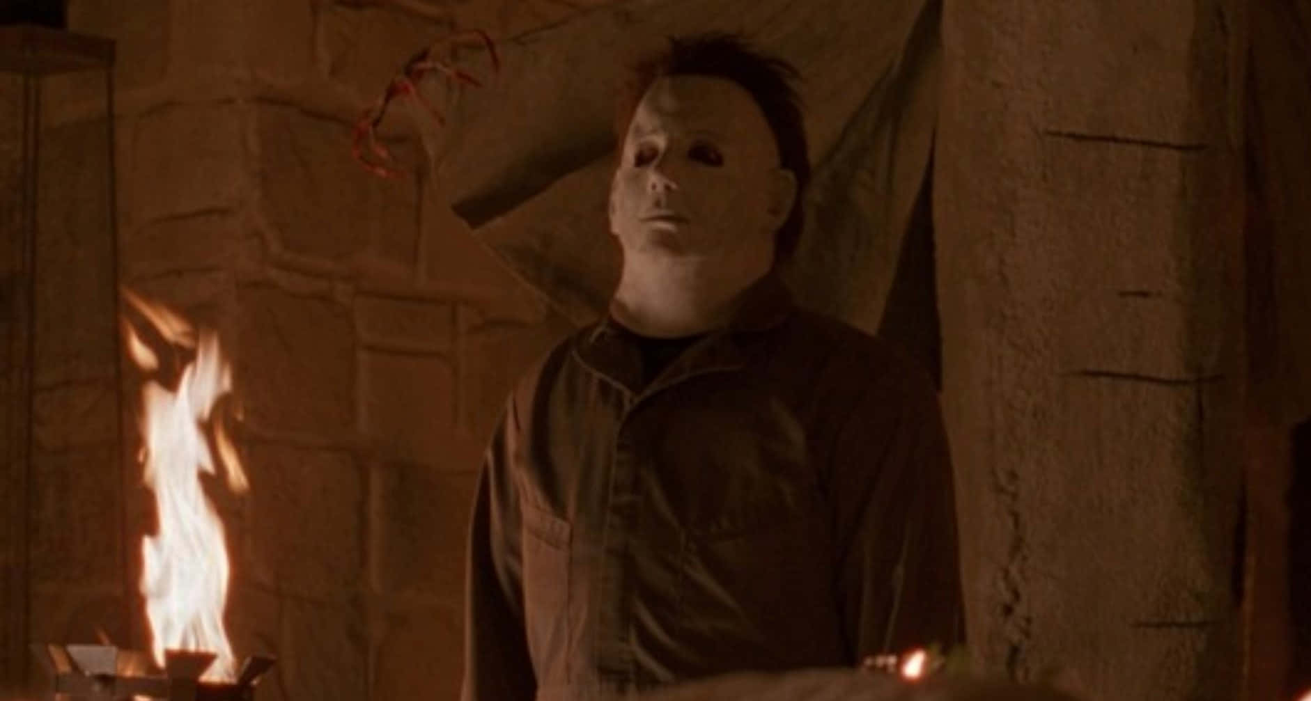 米高邁亞斯 桌布 壁紙 — Michael Myers 靜靜地站在昏暗的石室中，搖曳的火焰在牆上投射出詭異的影子。