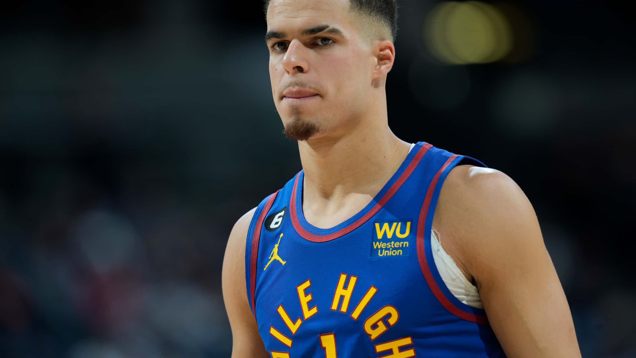 美國籃球員 Michael Porter Jr. 壁紙 — 一位身穿藍色丹佛金塊隊6號球衣的專注籃球運動員，在場館燈光下比賽期間凝視著。