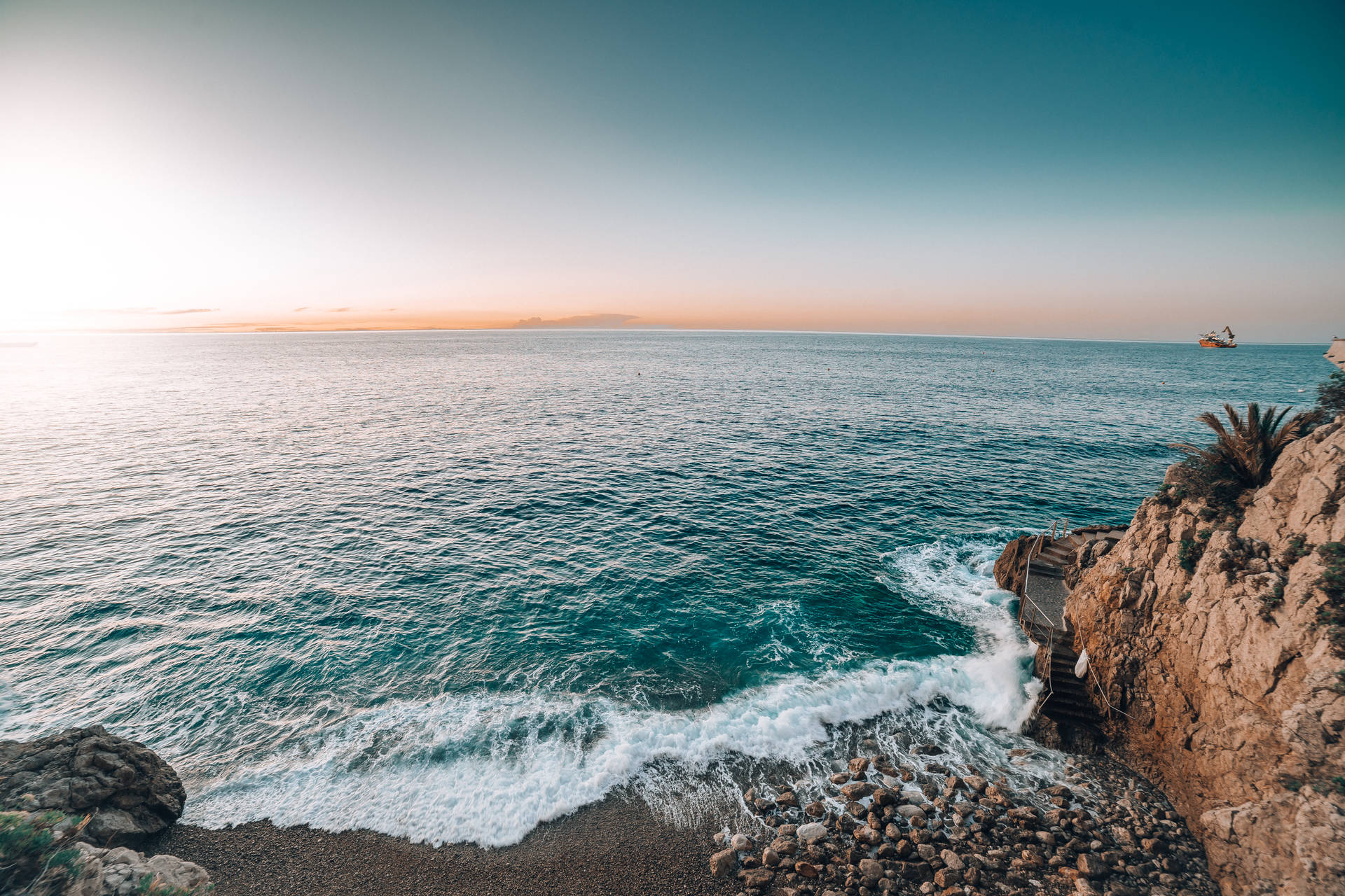 海上日落，海浪拍打岩石海岸，遠處有船