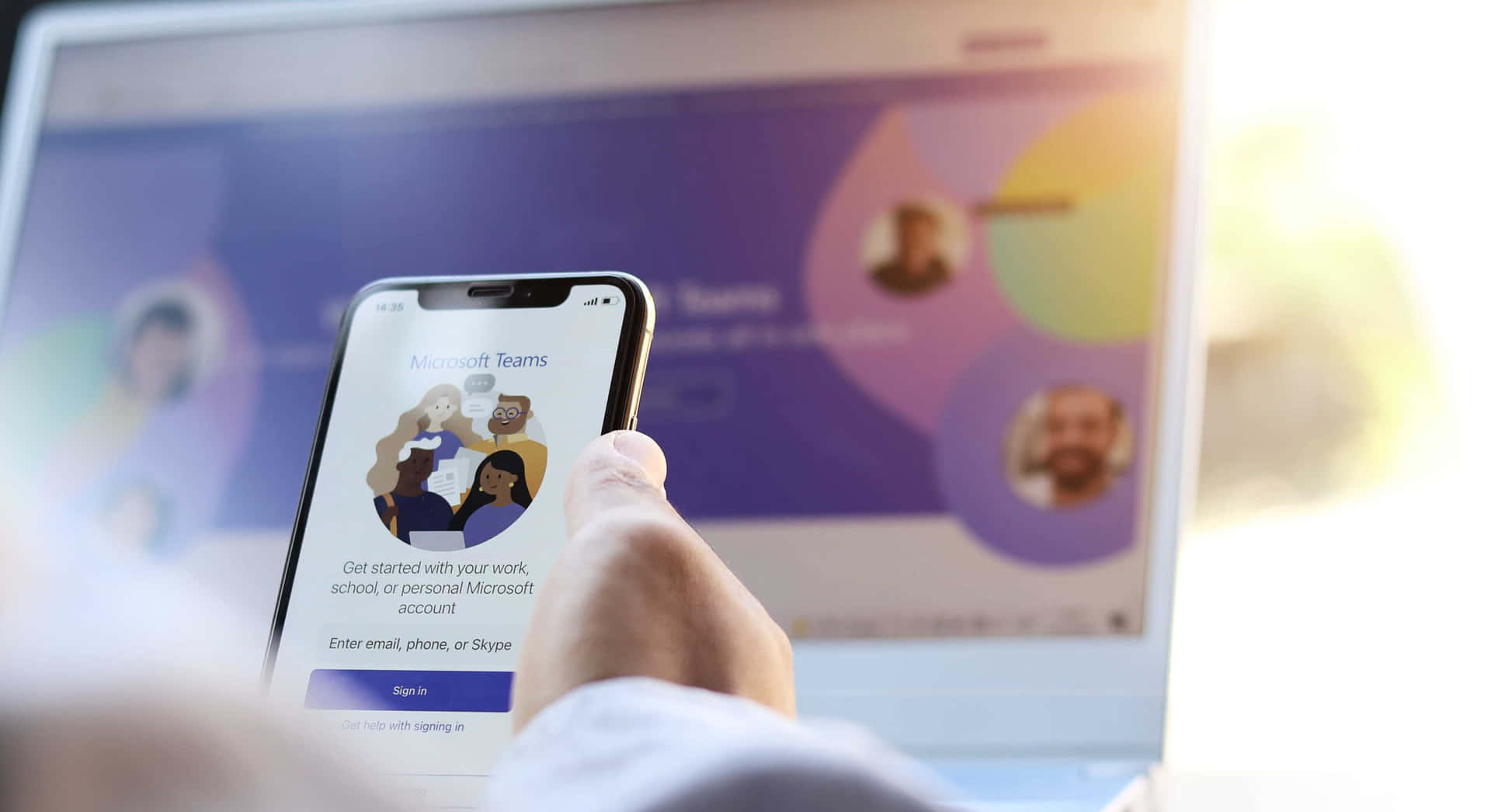 手拎住電話登入Microsoft Teams，背景有手提電腦。