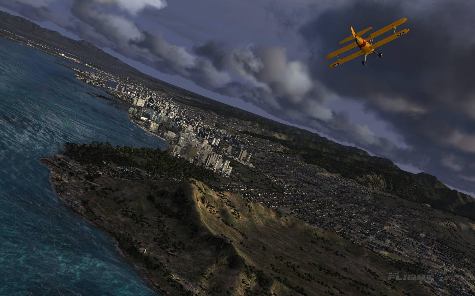 Microsoft 飛行模擬器 Stearman Model 壁紙 — 一架亮黃色雙翼機翱翔於坐落於海洋懸崖與暴風雲之間的海岸城市上空。