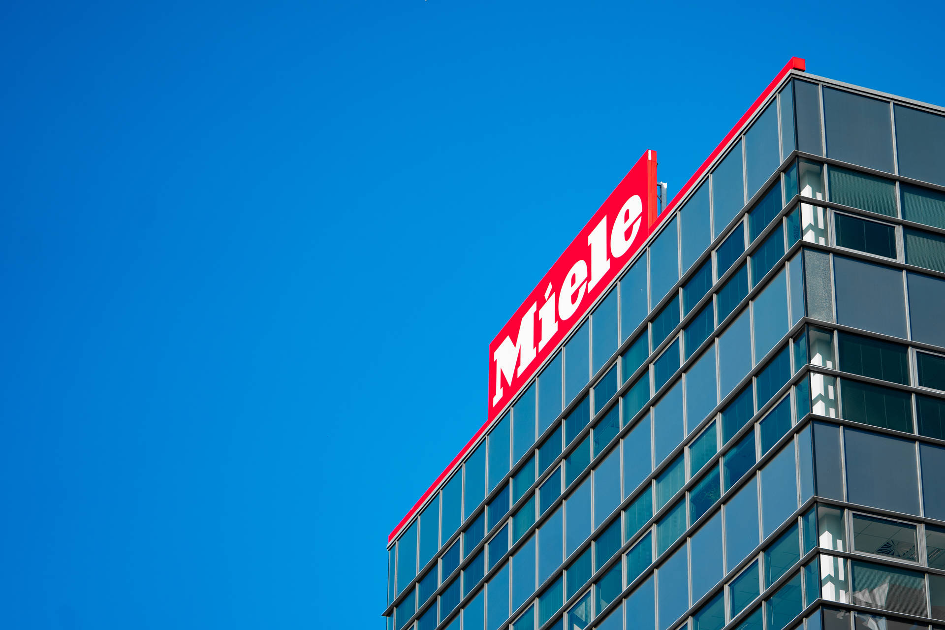 藍天下帶有紅色 Miele 標誌的現代玻璃建築