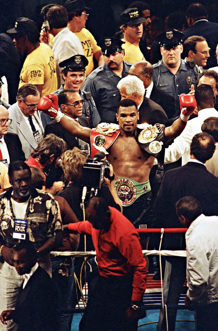 mike tyson 桌布 壁紙 — Mike Tyson 在擂台上高舉雙臂慶祝勝利，佩戴冠軍腰帶，被警察和媒體包圍。