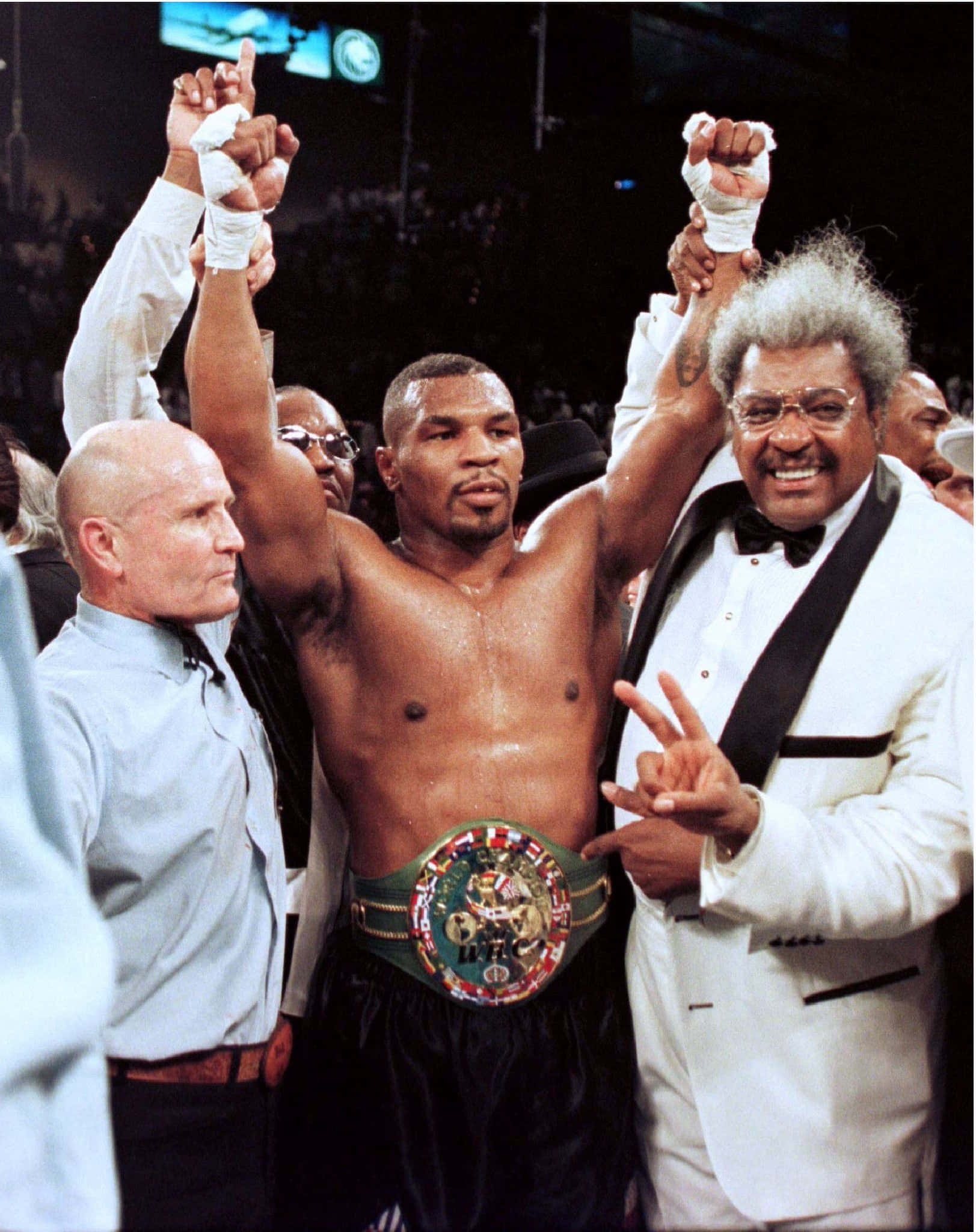 mike tyson 桌布 壁紙 — Mike Tyson 在擂台上高舉拳頭和冠軍腰帶慶祝勝利，官員和一位身穿燕尾服微笑的男子站在他兩旁。