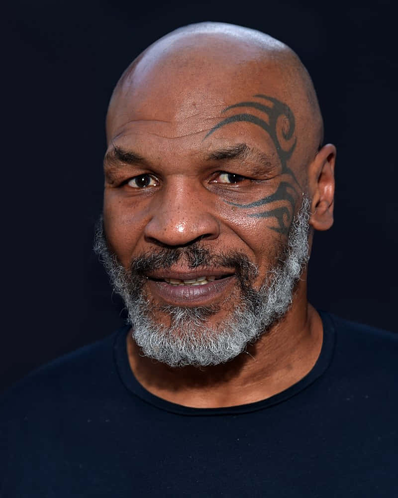 mike tyson 桌布 壁紙 — Mike Tyson 在深色背景下溫暖地微笑，他標誌性的部落紋身清晰可見於太陽穴。