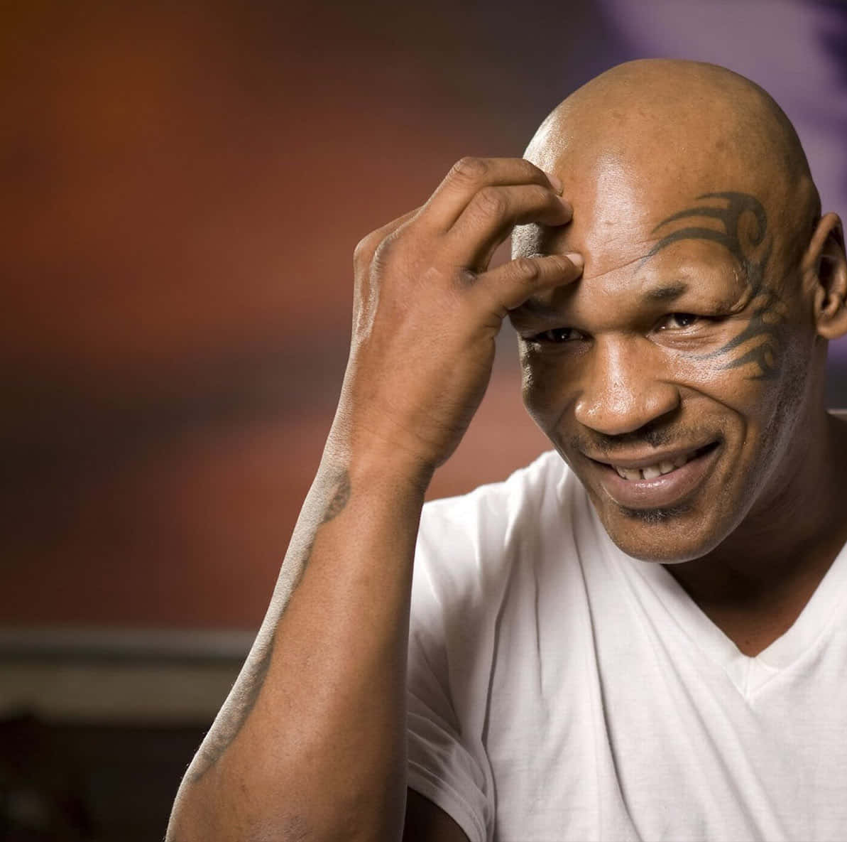 mike tyson 桌布 壁紙 — Mike Tyson 溫暖地微笑，同時用紋身的手觸摸額頭，背景是模糊的暖色調。