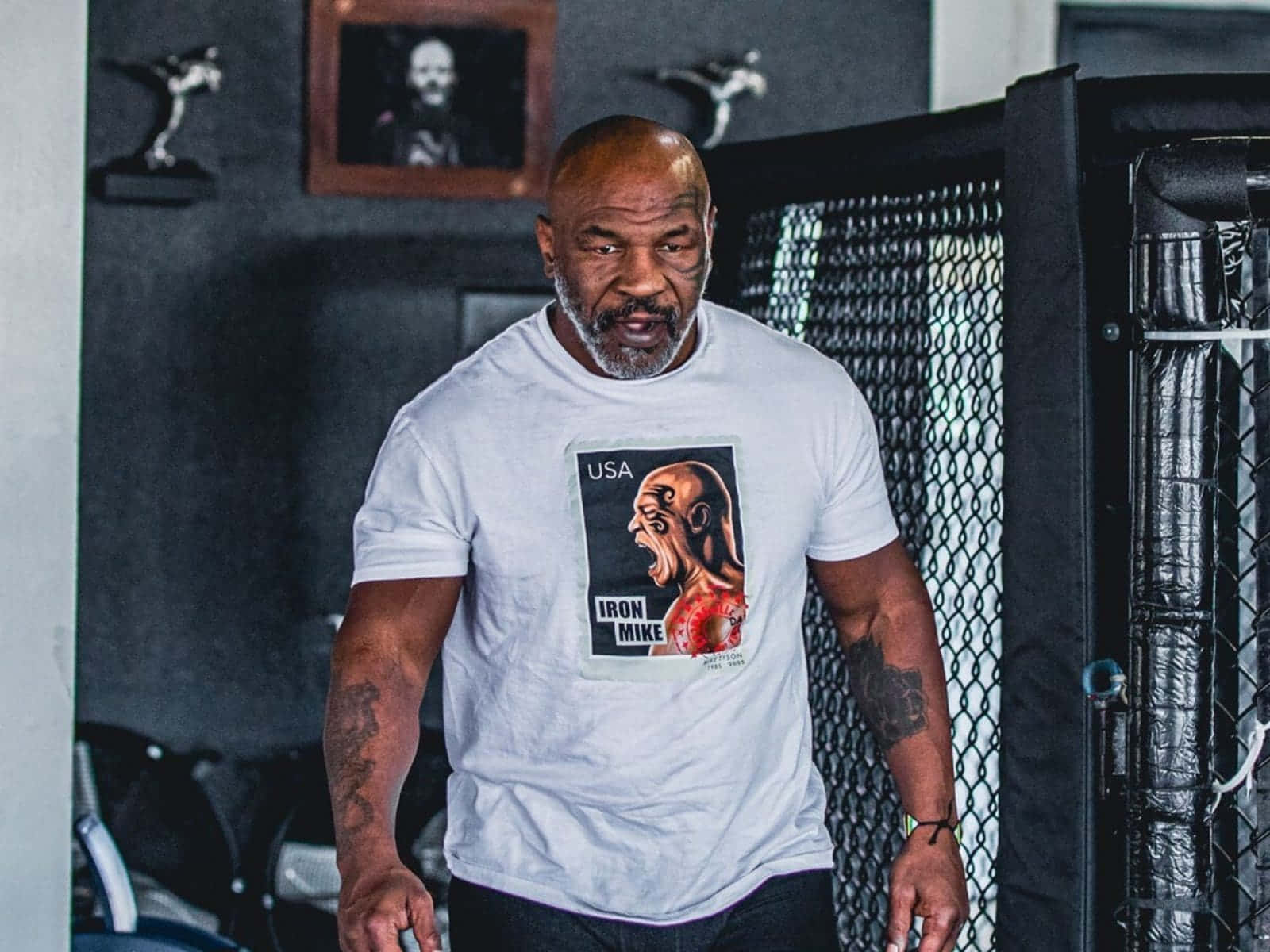 mike tyson 桌布 壁紙 — Mike Tyson 站在健身房，身穿印有「Iron Mike」圖案的白色T恤，手臂上的紋身清晰可見。