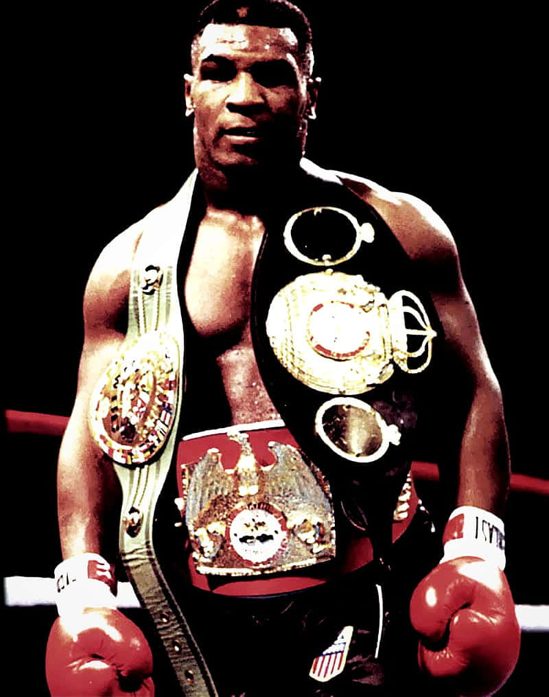 mike tyson 桌布 壁紙 — Mike Tyson 站在拳擊台上，佩戴多條冠軍腰帶和紅色手套，在戲劇性的聚光燈下。