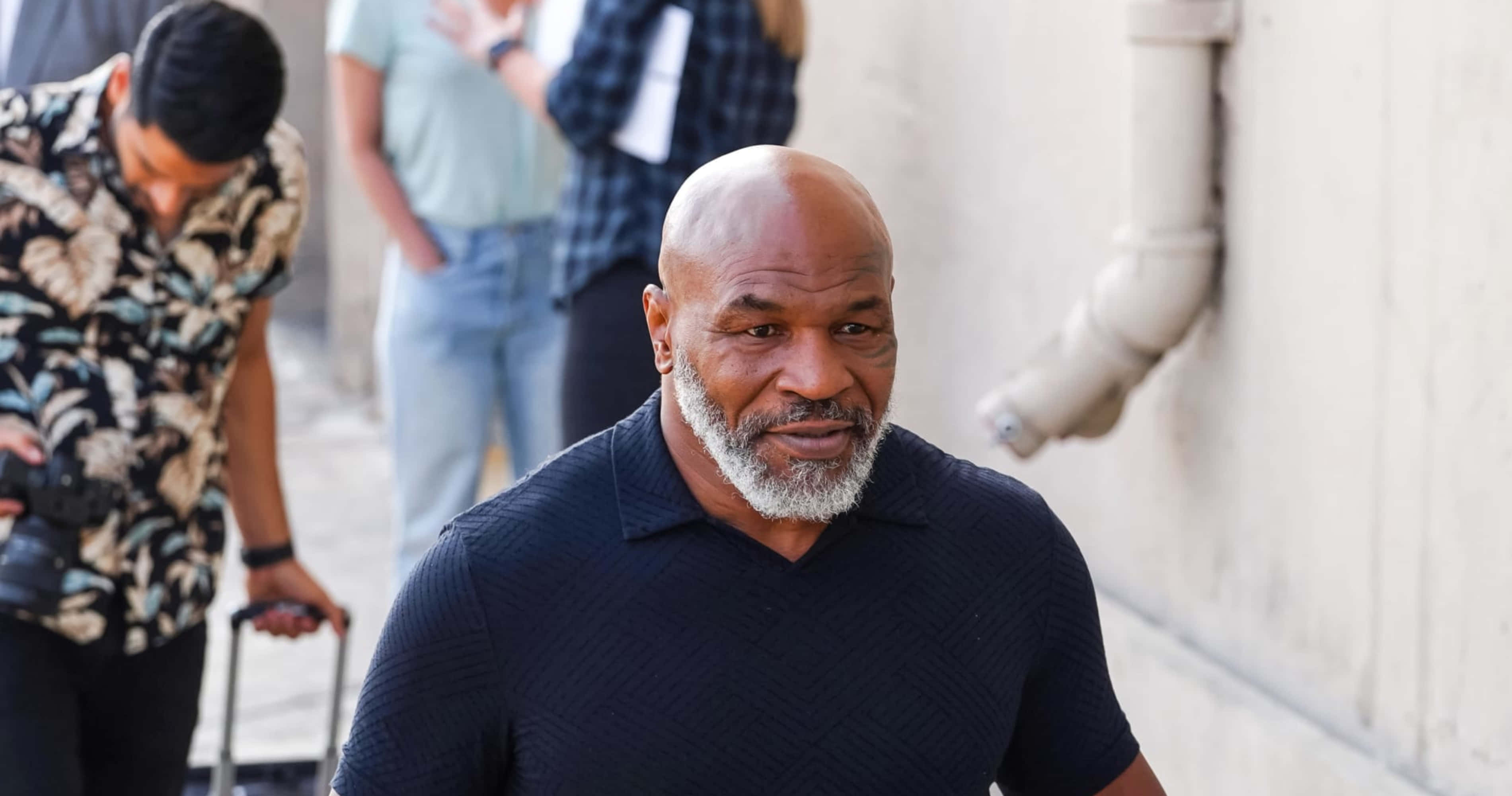 mike tyson 桌布 壁紙 — Mike Tyson 自信地走在陽光普照的城市小巷中，身後跟着一位攝影師。