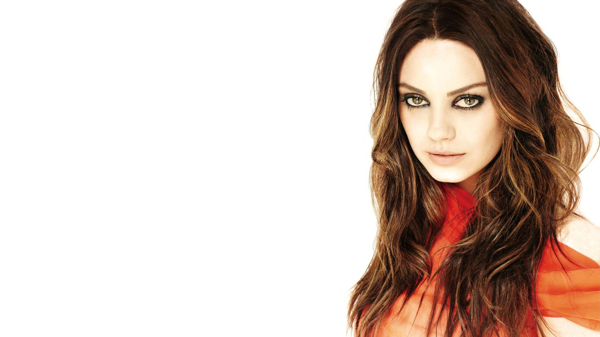 Mila Kunis穿橙色洋裝 壁紙 — 一位擁有長波浪棕色頭髮和引人注目的綠色眼睛的女性，在純白色背景前直視鏡頭。