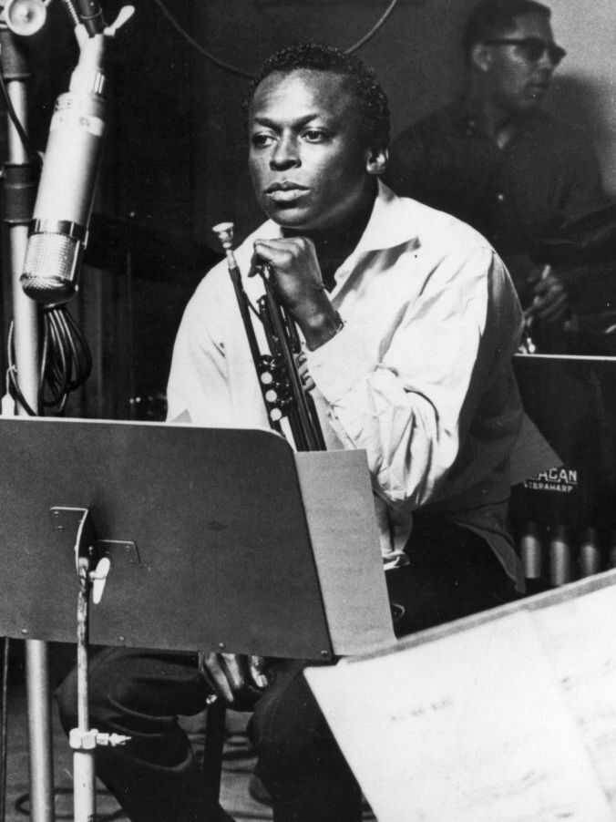 著名男小號手Miles Davis 壁紙 — 一位爵士小號手坐在錄音室中，手持樂器，附近有麥克風的黑白肖像。