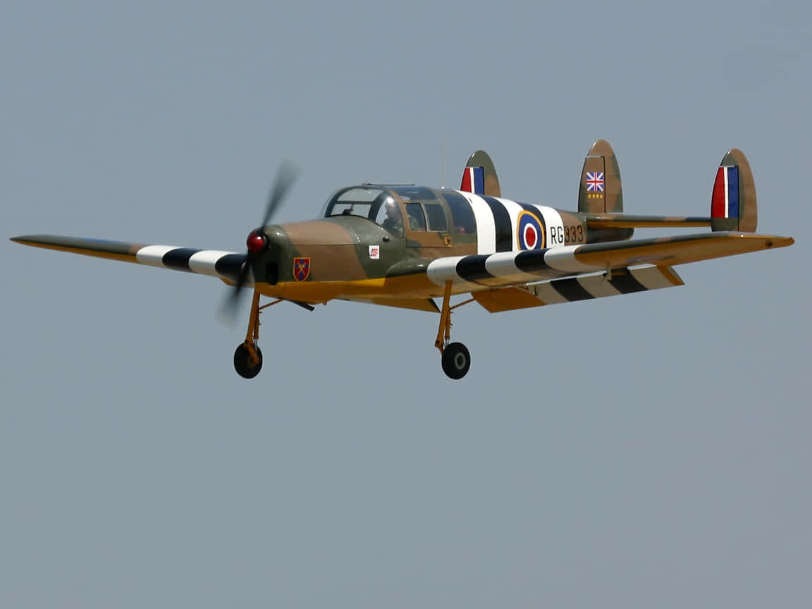 Miles M.38 Messenger 小型飛機 壁紙 — 一架帶有迷彩和圓形標誌的復古軍用教練機在清澈的淡藍色天空中翱翔。