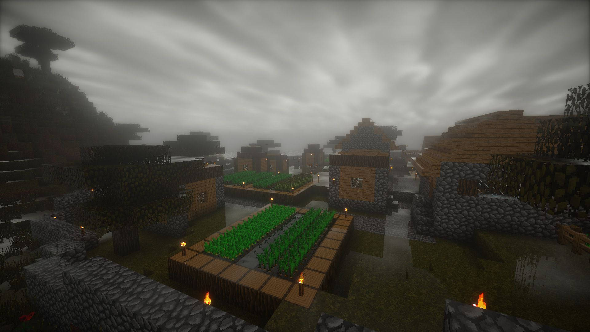 Minecraft PC 阴鬱農場 壁紙 — 一個霧氣瀰漫的Minecraft村莊，有木屋、石牆和火把在陰天天空下發光。