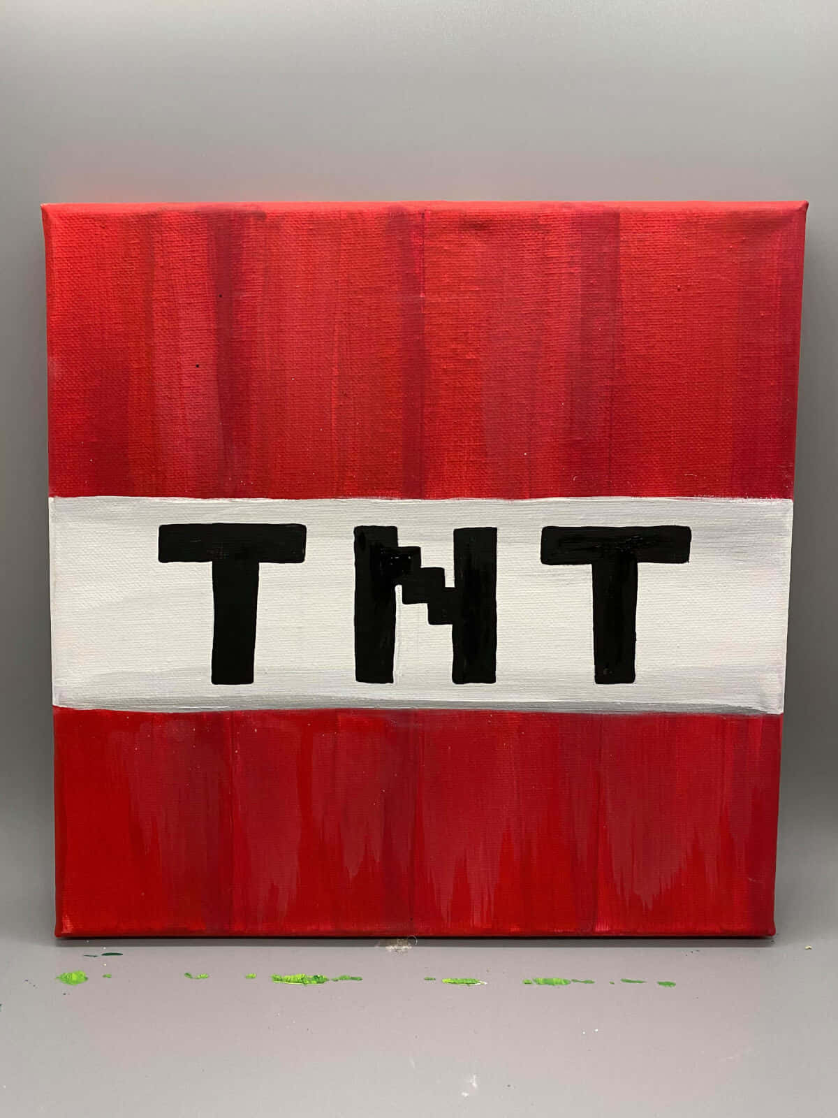 用 Minecraft TNT 創造毀滅 壁紙 — 一幅大膽的紅白畫布，上面有黑色的「TNT」字母，顯示筆觸和地板上的綠色油漆飛濺。