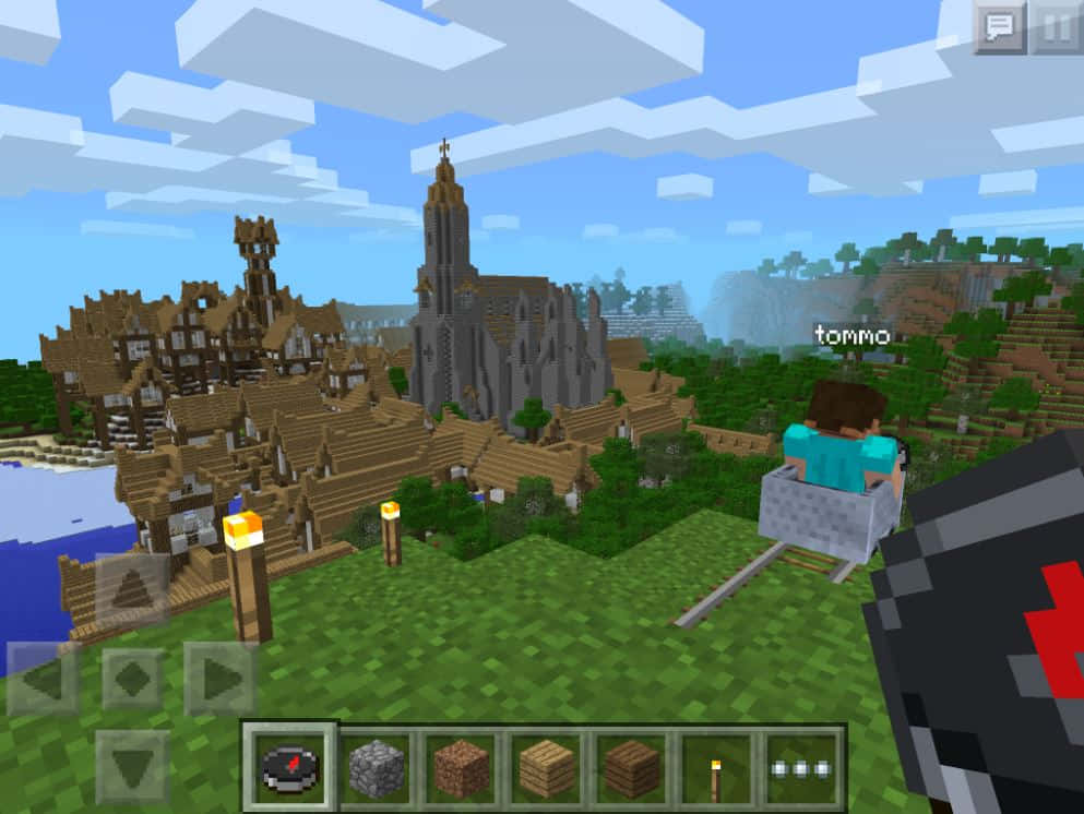 Minecraft Pocket Edition 桌布 壁紙 — Minecraft 玩家乘坐礦車經過一個中世紀村莊，村莊內有一座高聳的教堂，背景是方塊狀的藍天。