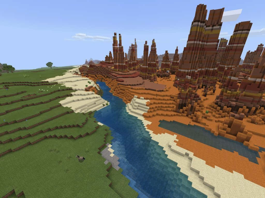 Minecraft Bedrock Edition 桌布 壁紙 — Minecraft 風景，蜿蜒的河流將鬱鬱蔥蔥的綠色平原與高聳的紅褐色峽谷分隔開來，天空清澈湛藍。